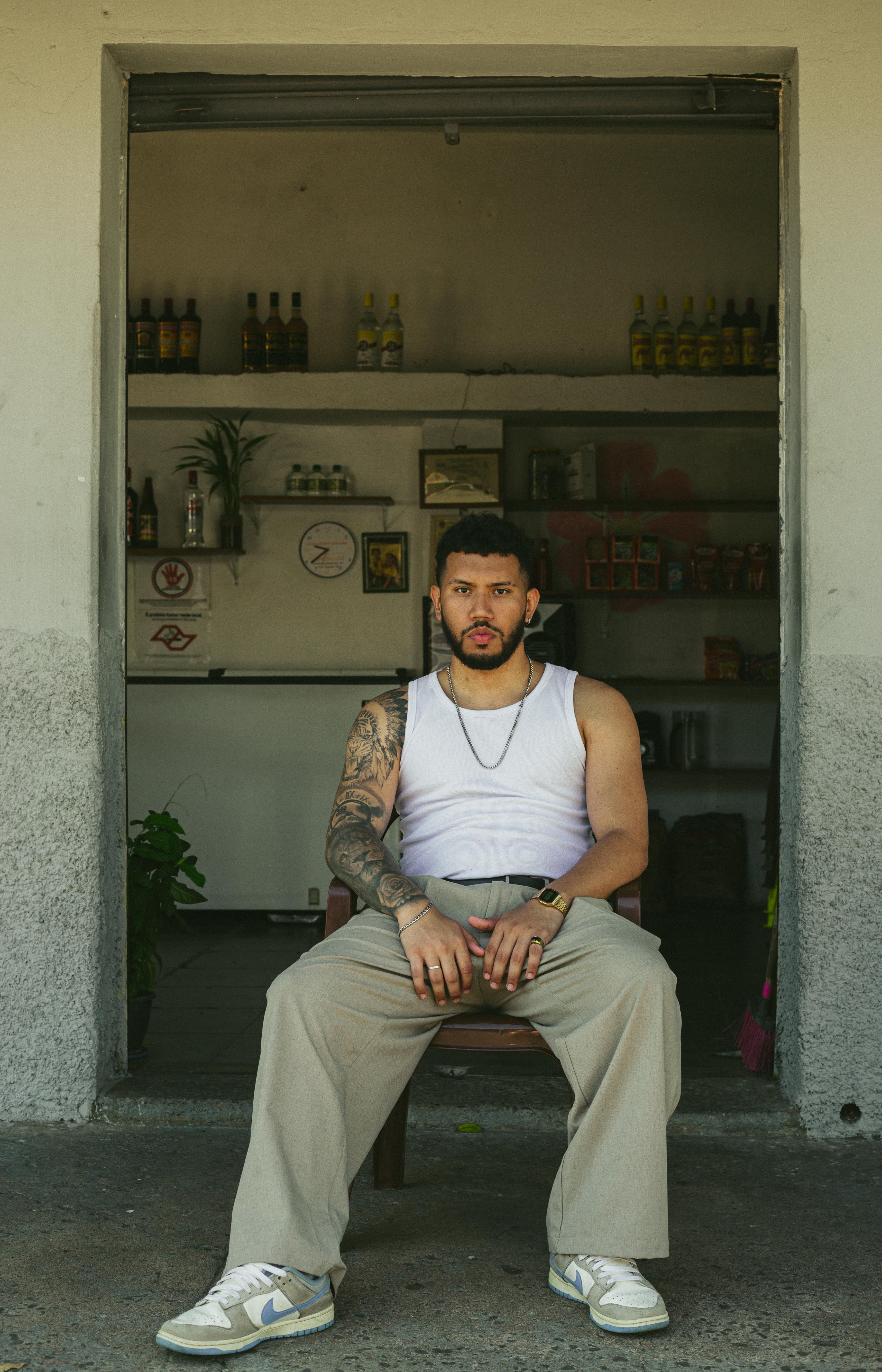 Tattooed man in a white tank top sitting outdoors in São Paulo.