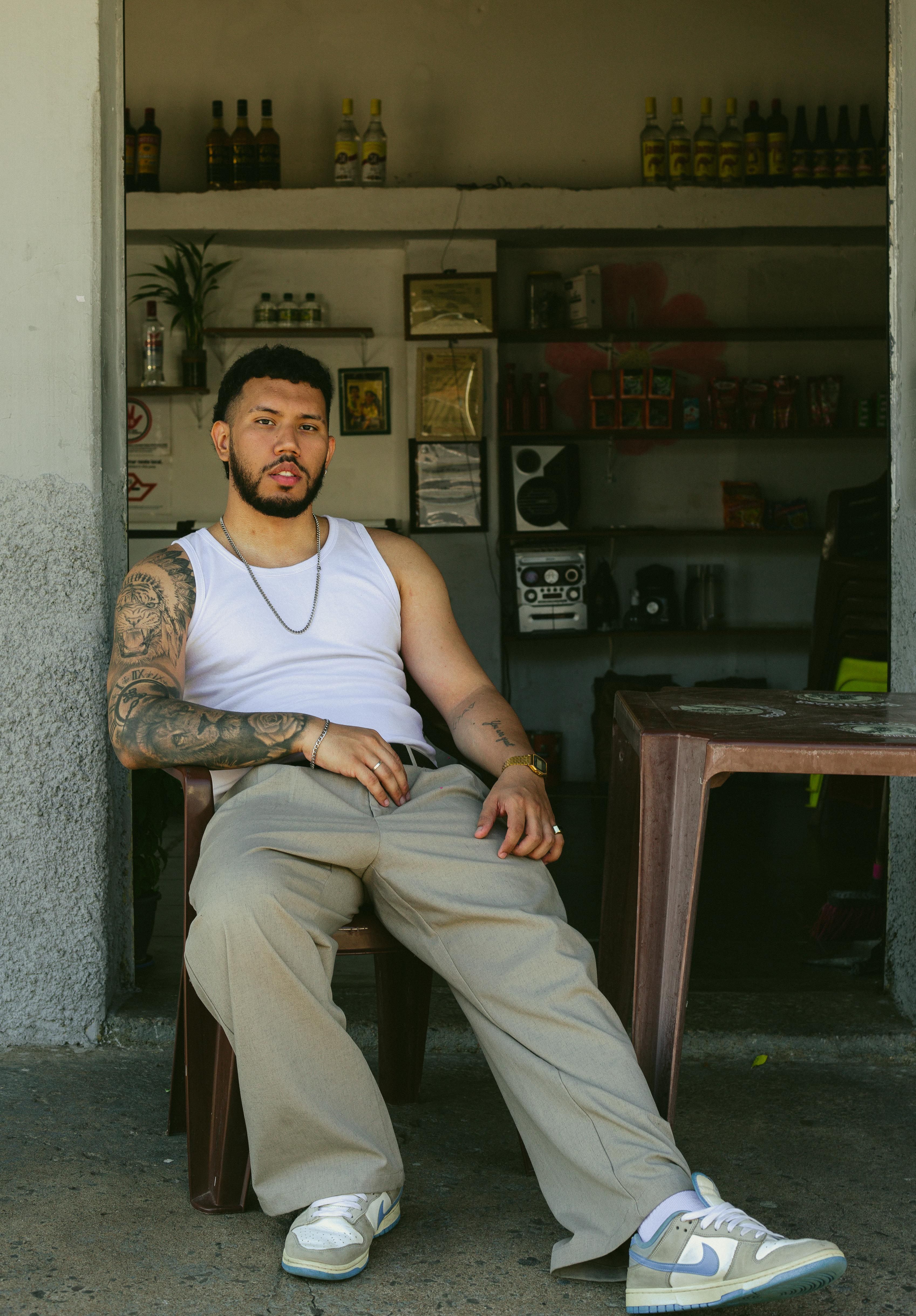 Stylish portrait of a tattooed man in streetwear sitting at an outdoor bar in São Paulo, Brazil.