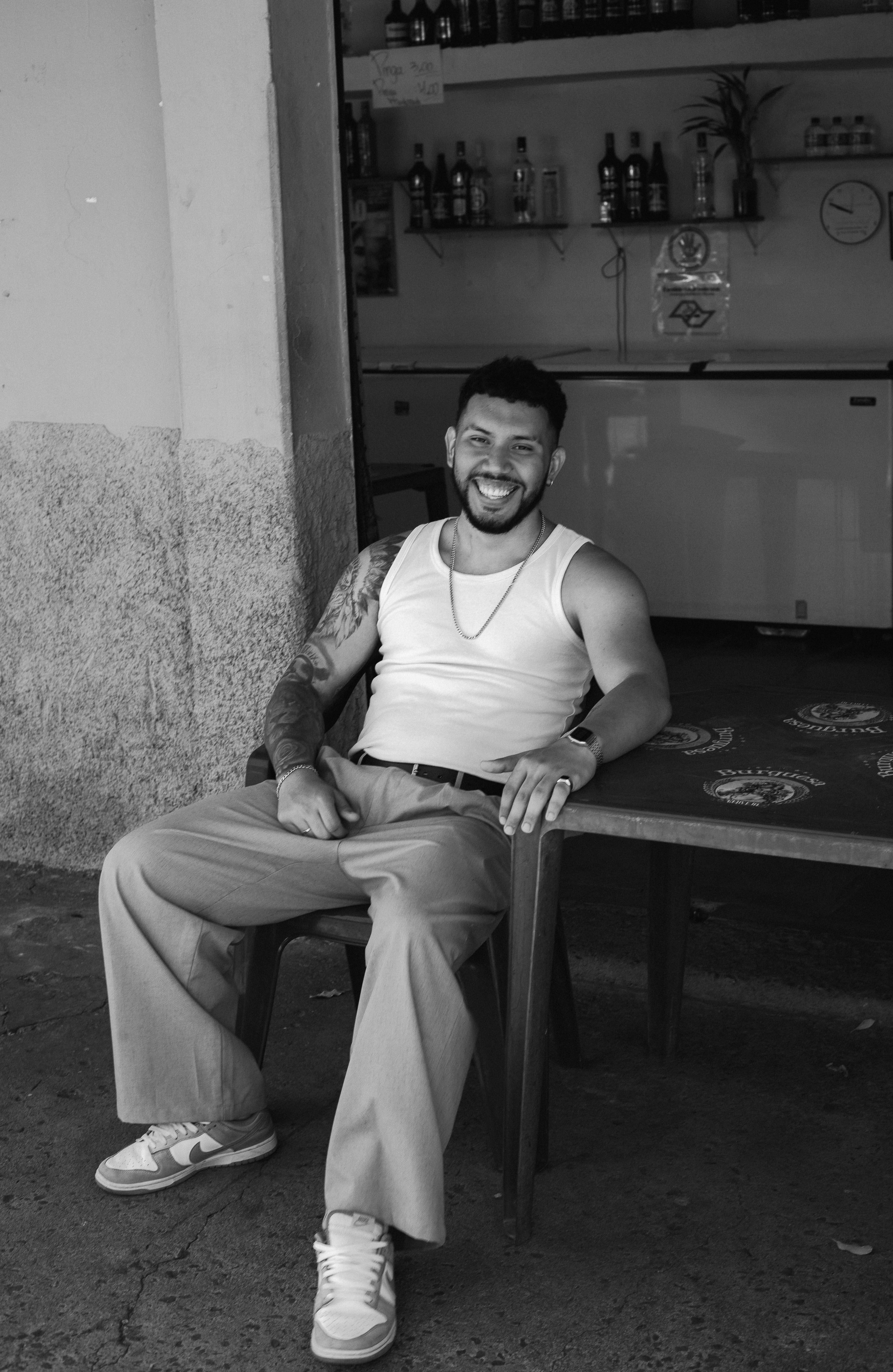 Portrait of a smiling man in casual attire sitting outdoors at a bar in Presidente Prudente, Brazil.