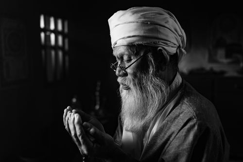 Free A contemplative elderly man in traditional attire praying indoors in black and white. Stock Photo