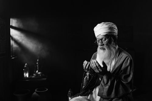 Free A senior man in traditional attire meditates with prayer beads, bathed in light. Stock Photo