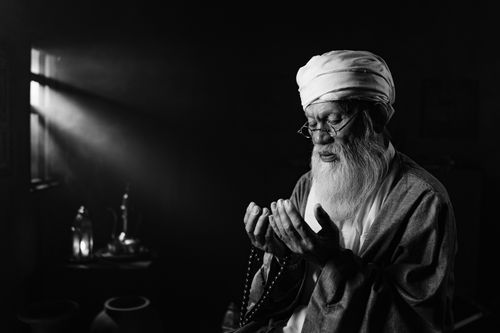 Free Black and white portrait of an elderly man deep in prayer holding prayer beads with soft window light. Stock Photo
