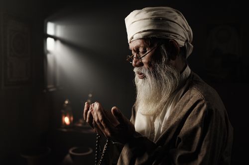 Free Elderly man with a white beard and traditional attire praying indoors. Peaceful and spiritual scene. Stock Photo