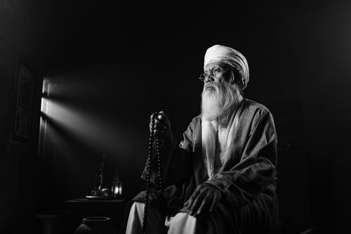 Free An elderly man with a turban sits praying with mala beads in a serene, indoors setting. Stock Photo