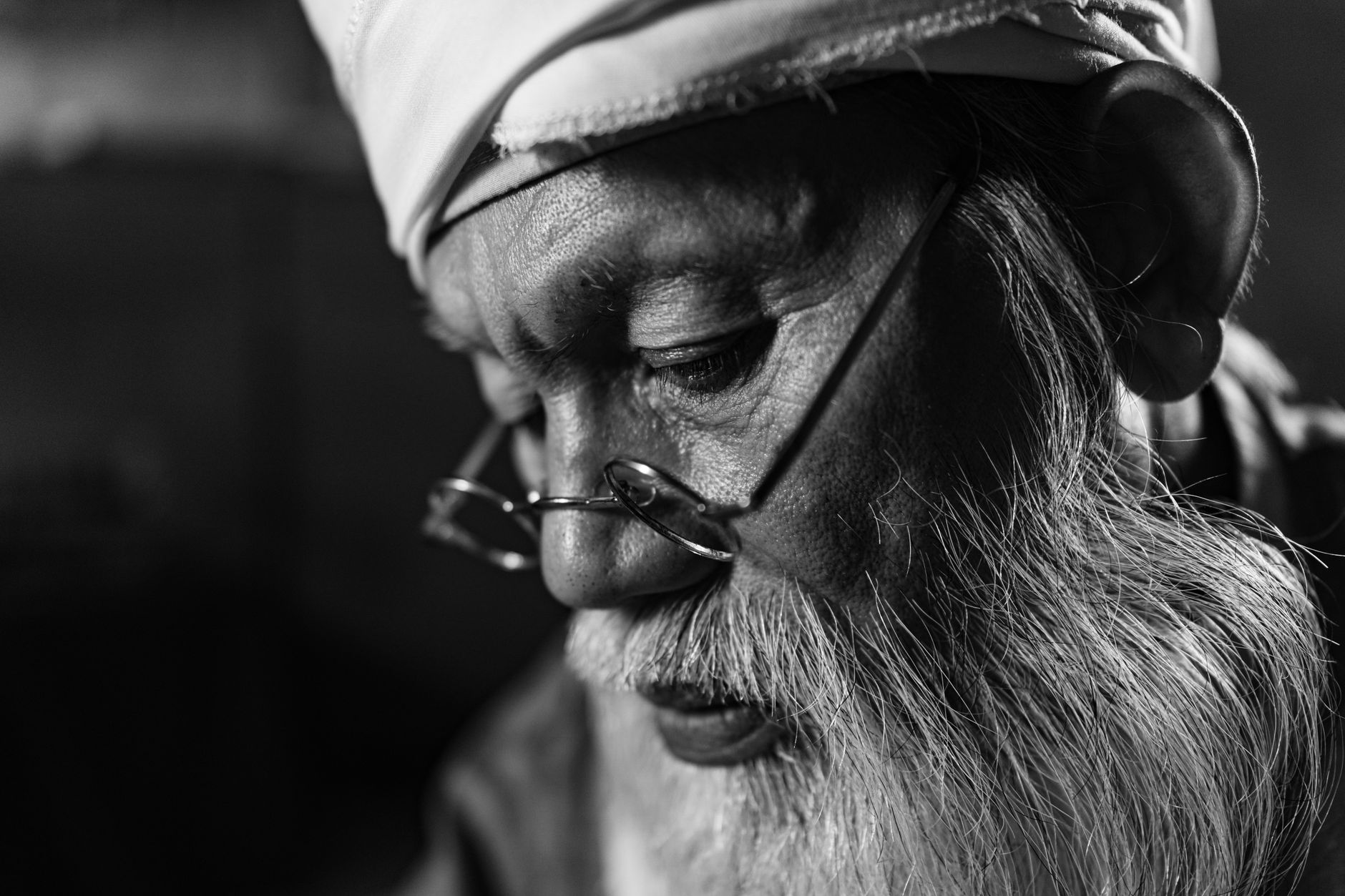 Black and white close-up portrait of an elderly man wearing glasses and traditional headwear.