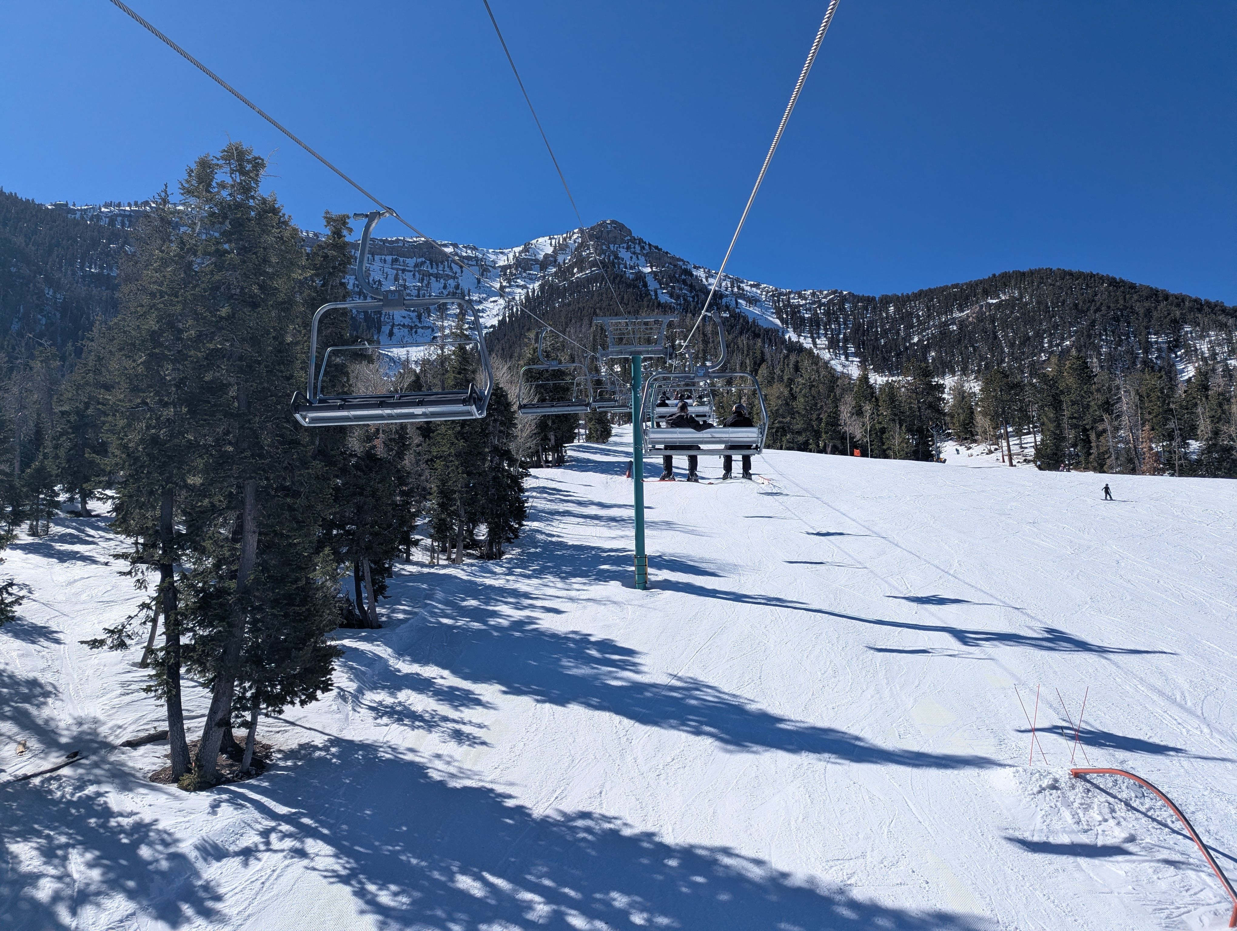 ski lifts over alpine bowl, groomed pistes, clear blue sky