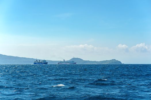 Two ferries sail on the ocean with distant islands under a clear blue sky.