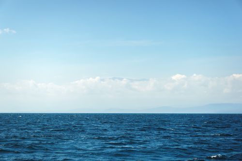 Free A serene seascape featuring calm ocean waters under a bright blue sky with fluffy clouds. Stock Photo