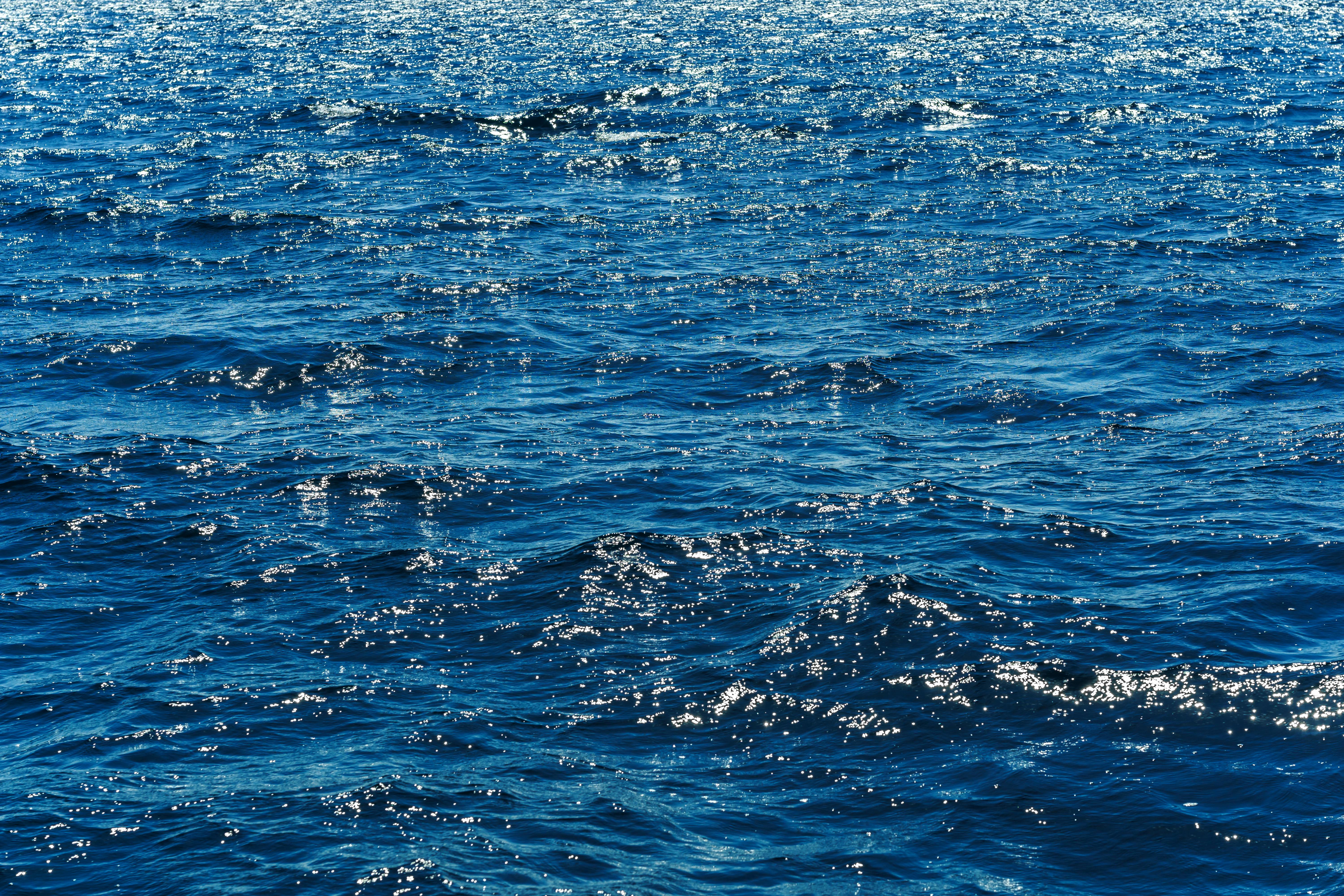Ücretsiz Güneş ışığıyla aydınlanan okyanus dalgaları, berrak gökyüzü altında derin mavi tonlarını ve ışıltılı yansımalarını sergiliyor. Stok Fotoğraflar