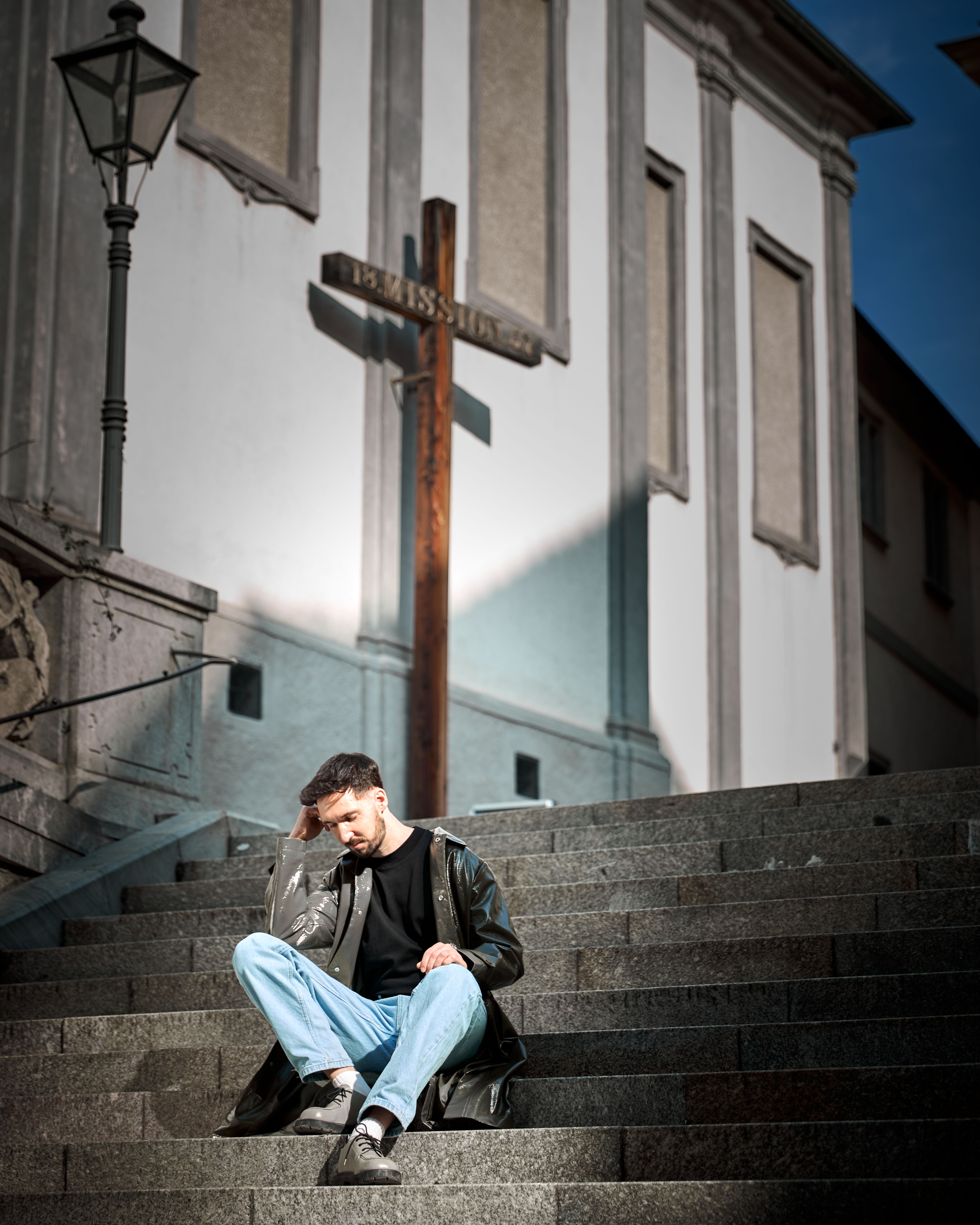 Man sitting thoughtfully on church steps with cross in Graz, Austria.