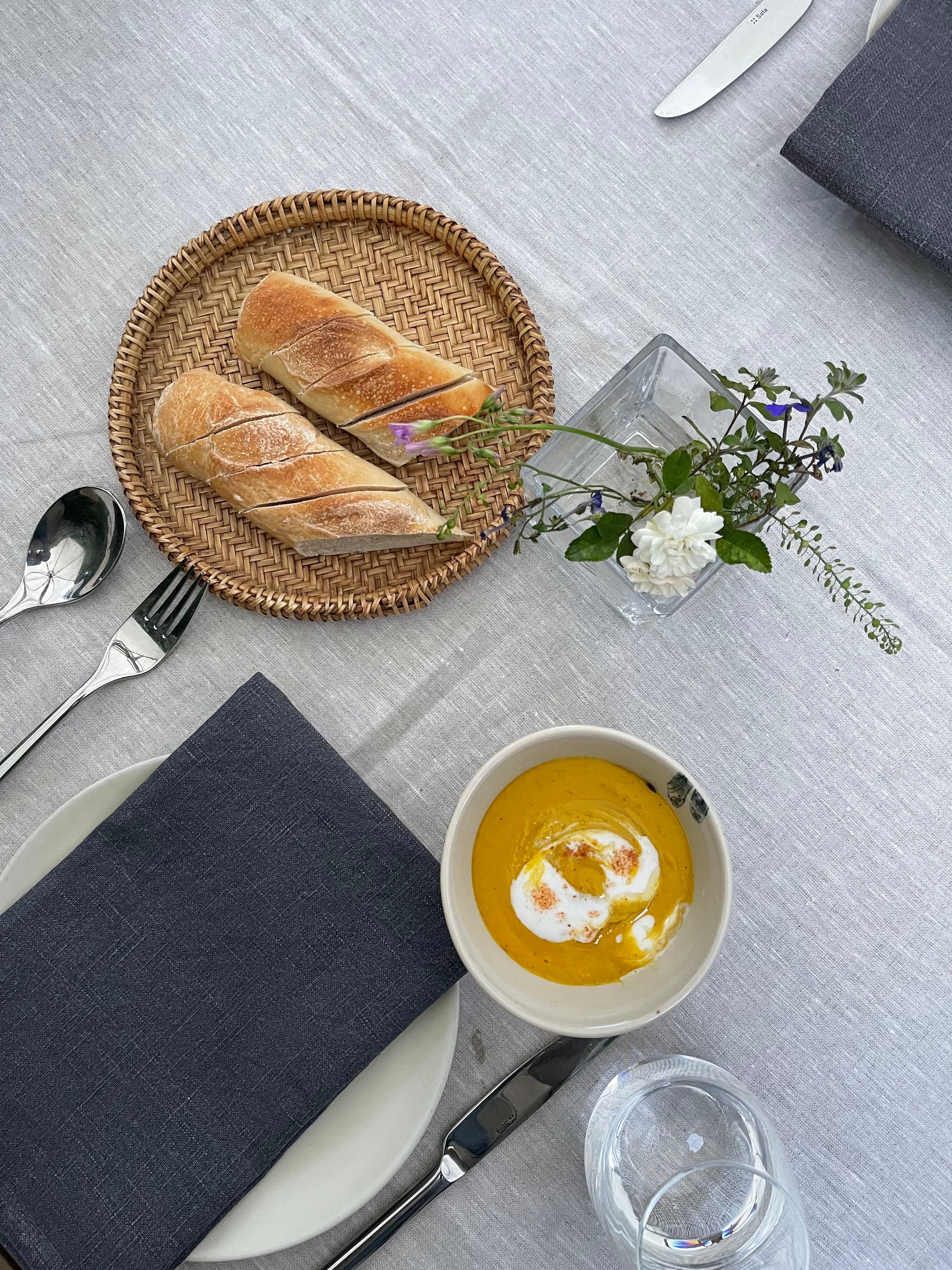 A sophisticated table setup featuring bread on a wicker plate and a bowl of pumpkin soup, perfect for a cozy meal.