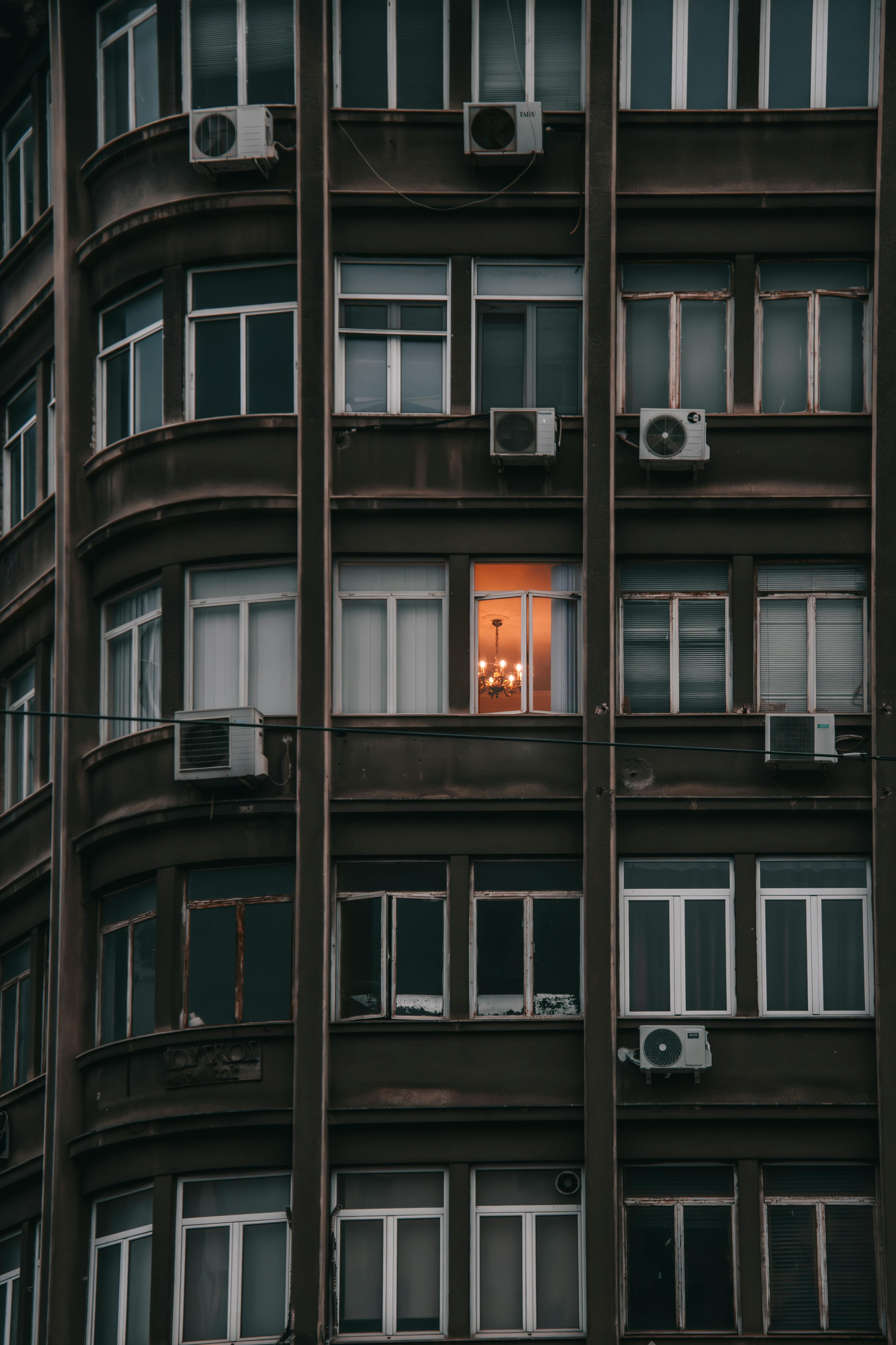 Ücretsiz Şehirdeki bir apartman binasının cephesinde, aydınlatılmış tek bir pencere, kentsel zıtlıkları sergiliyor. Stok Fotoğraflar