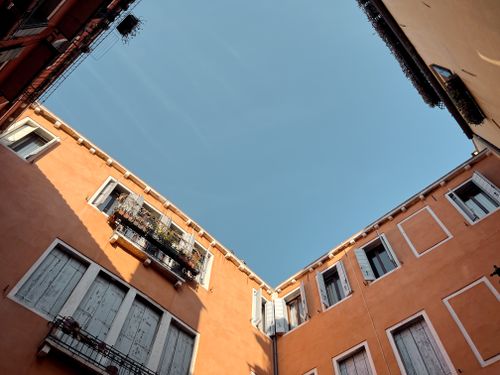 Free View of traditional Venetian architecture in a sunlit courtyard, framed by warm orange facades and clear blue sky. Stock Photo