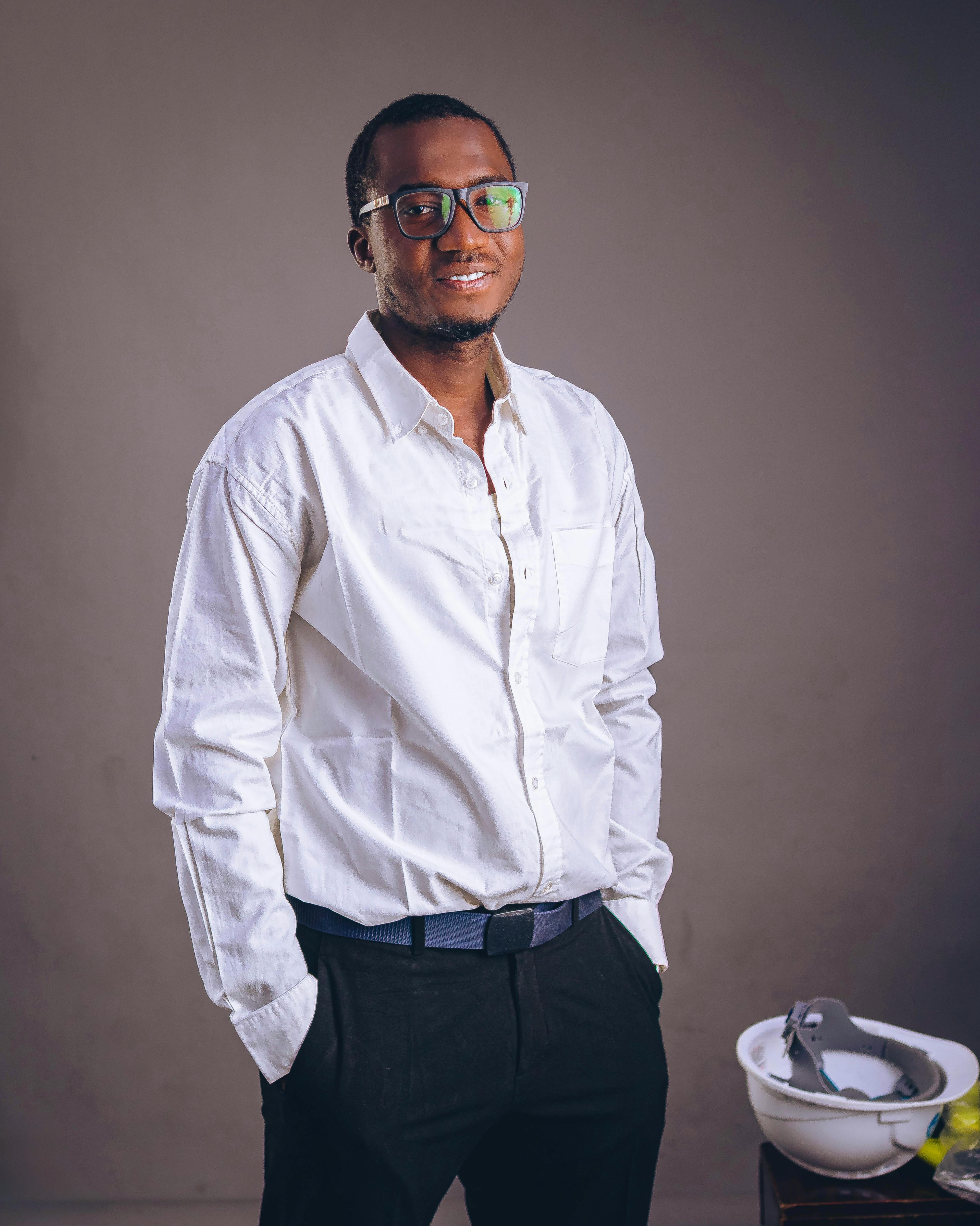 Portrait of a confident young adult male wearing glasses and a white shirt, standing indoors.