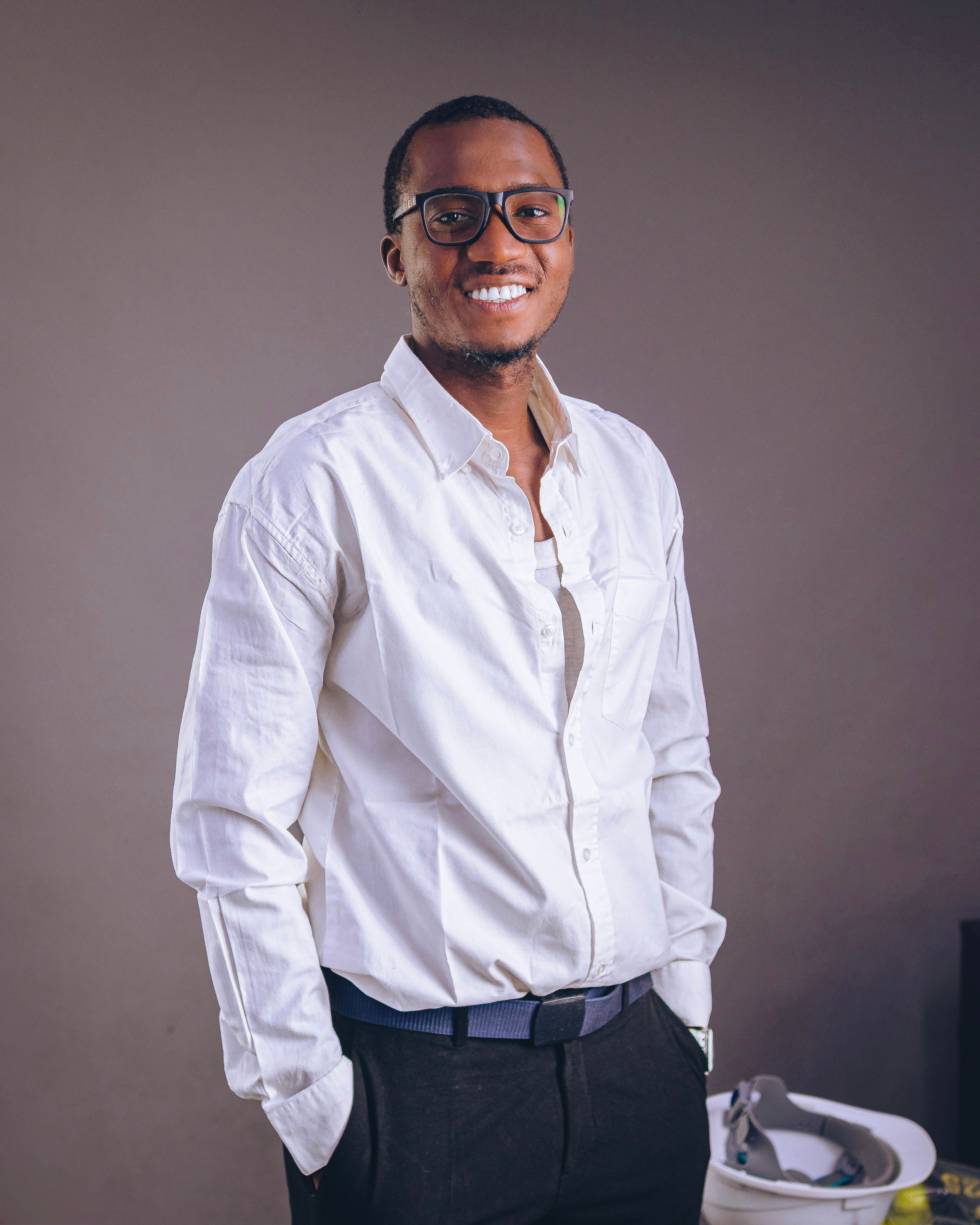 Portrait of a smiling African man in a casual white shirt and glasses, standing indoors. Ideal for lifestyle themes.