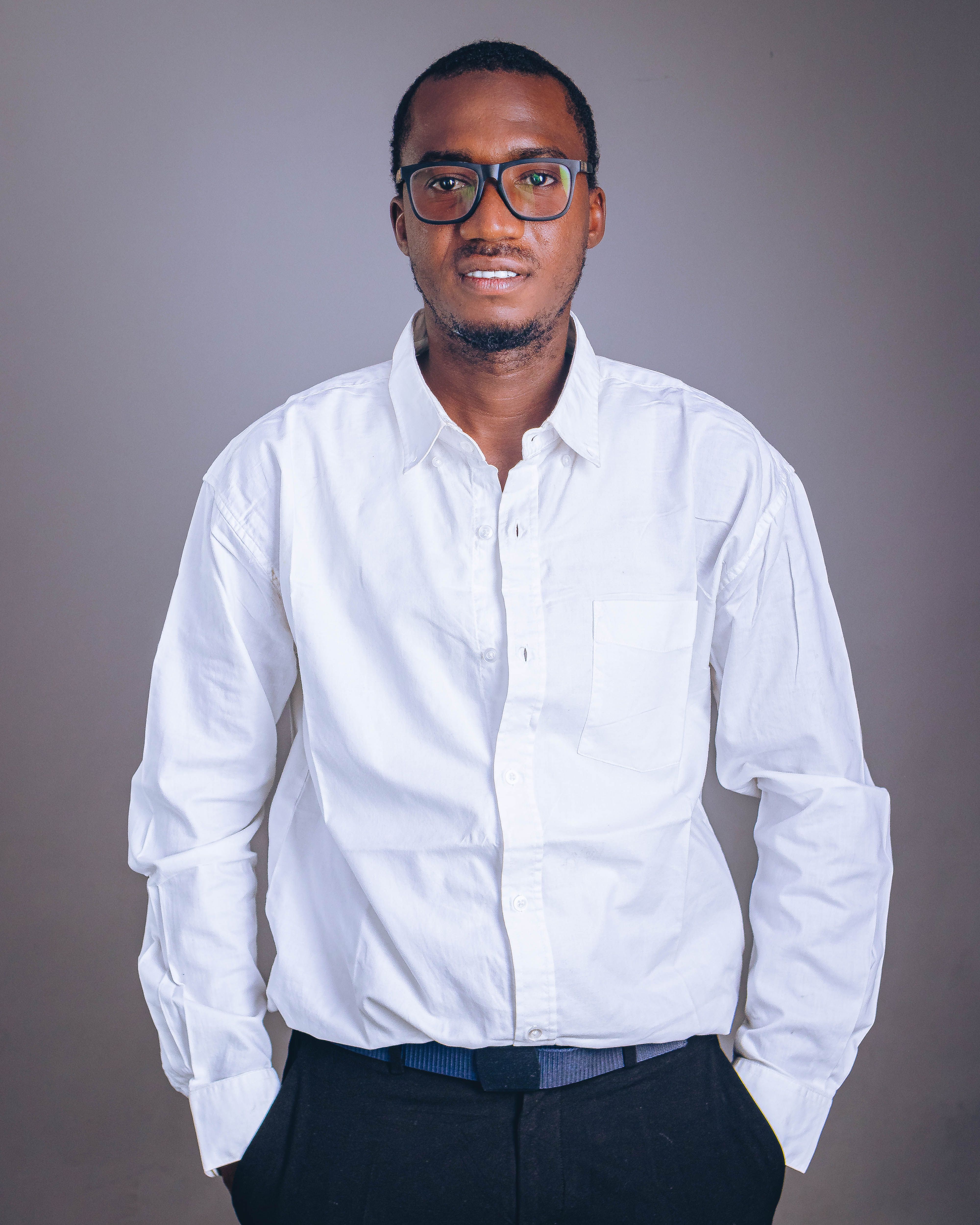 Portrait of a confident young man wearing a white shirt and glasses, standing against a neutral background.