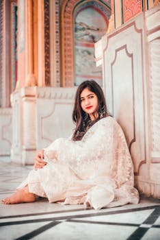 一位身着印度传统服装、涂着红色口红的年轻女子，正坐在斋浦尔的建筑环境中