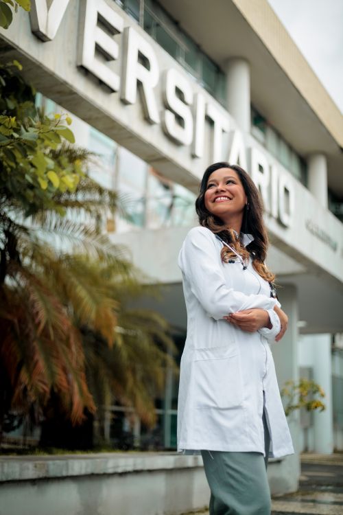 Free Smiling female doctor in white coat standing outdoors near university building, expressing confidence and optimism. Stock Photo
