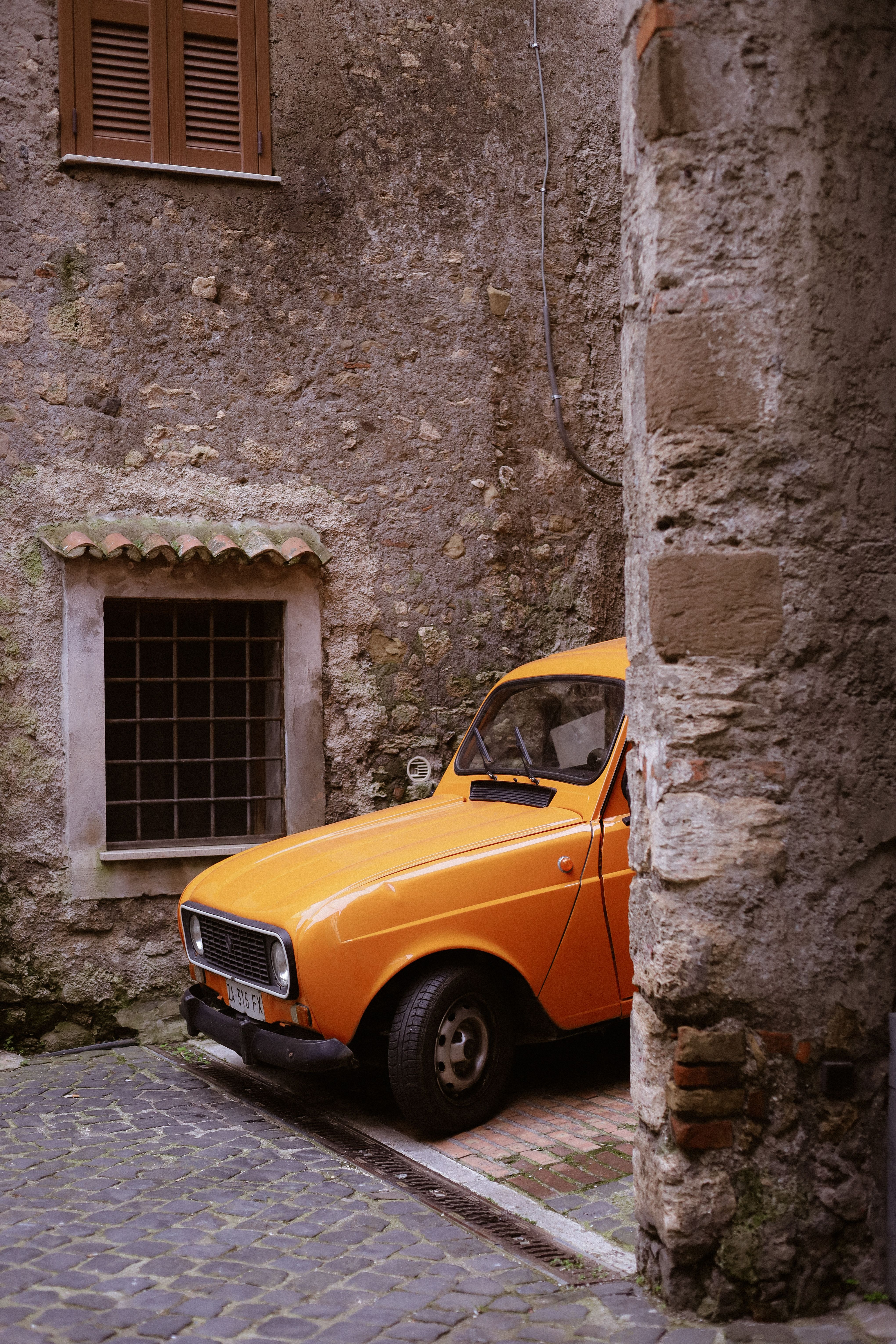 A classic orange car in a rustic alley of Anagni, Lazio, Italy. Perfect for vintage themes.
