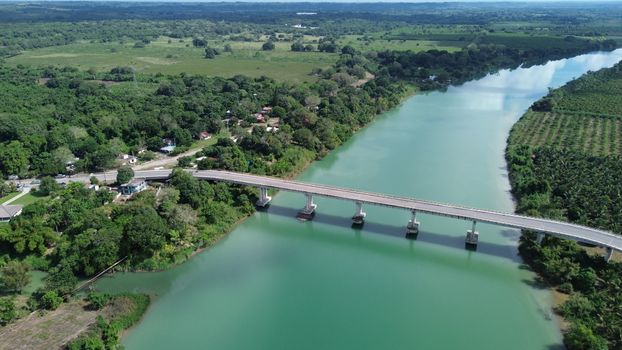 Aerial view of a scenic bridge crossing a tropical river surrounded by lush green landscape.