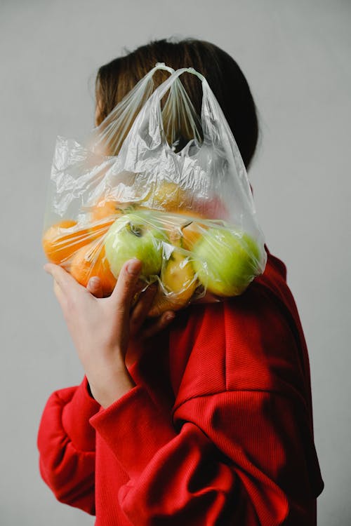 Person Carrying A Plastic Bag Full Of Fruits