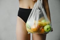 一个穿着黑色短裤的人拿着装满各种新鲜水果的塑料袋，强调浪费和回收