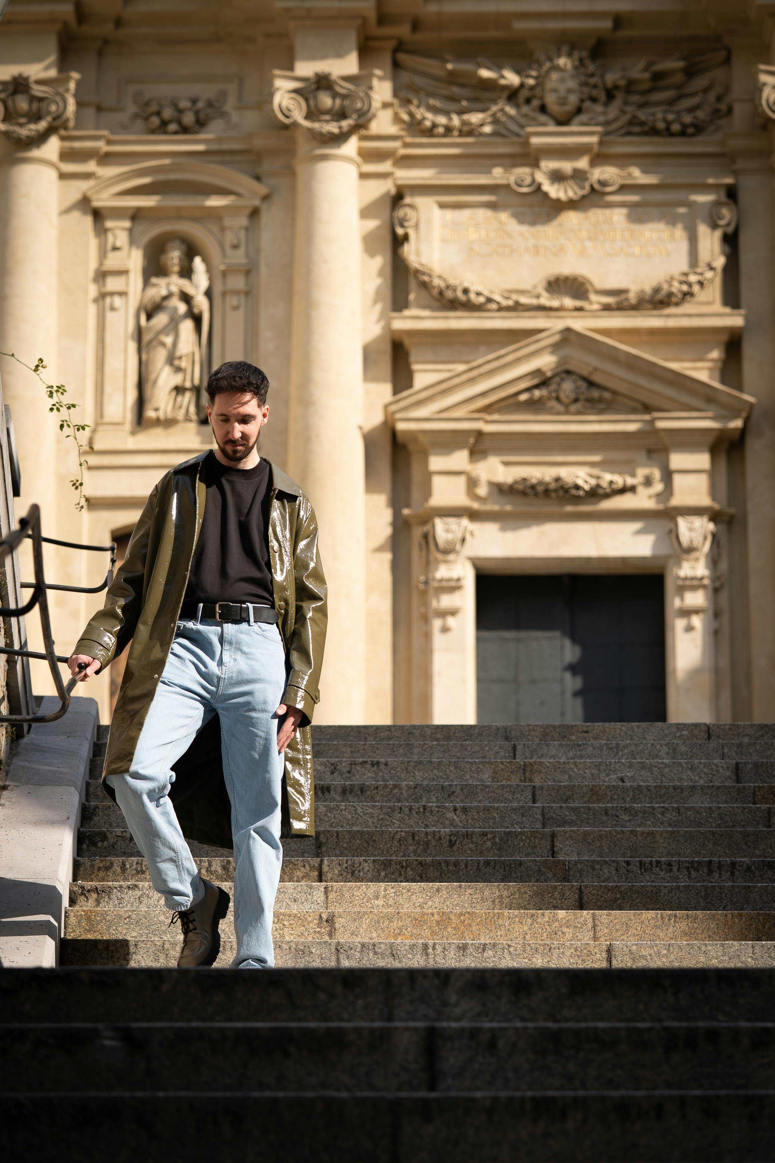 A fashionable man in a coat walks down steps outside a historic building in Graz, Austria.