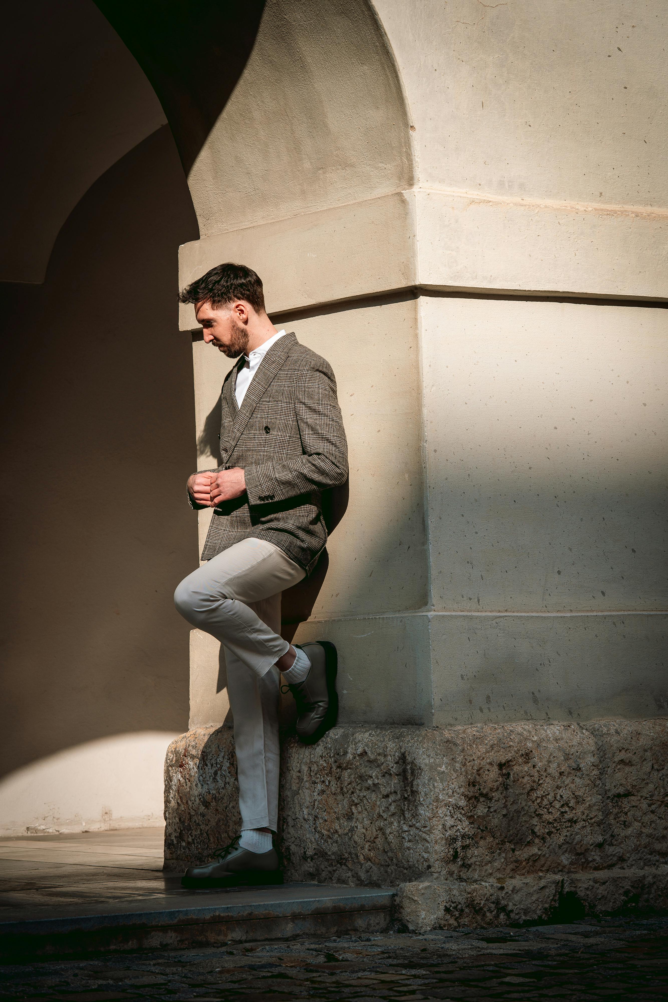 A fashionable male stands elegantly against a historic archway in Graz, Austria.