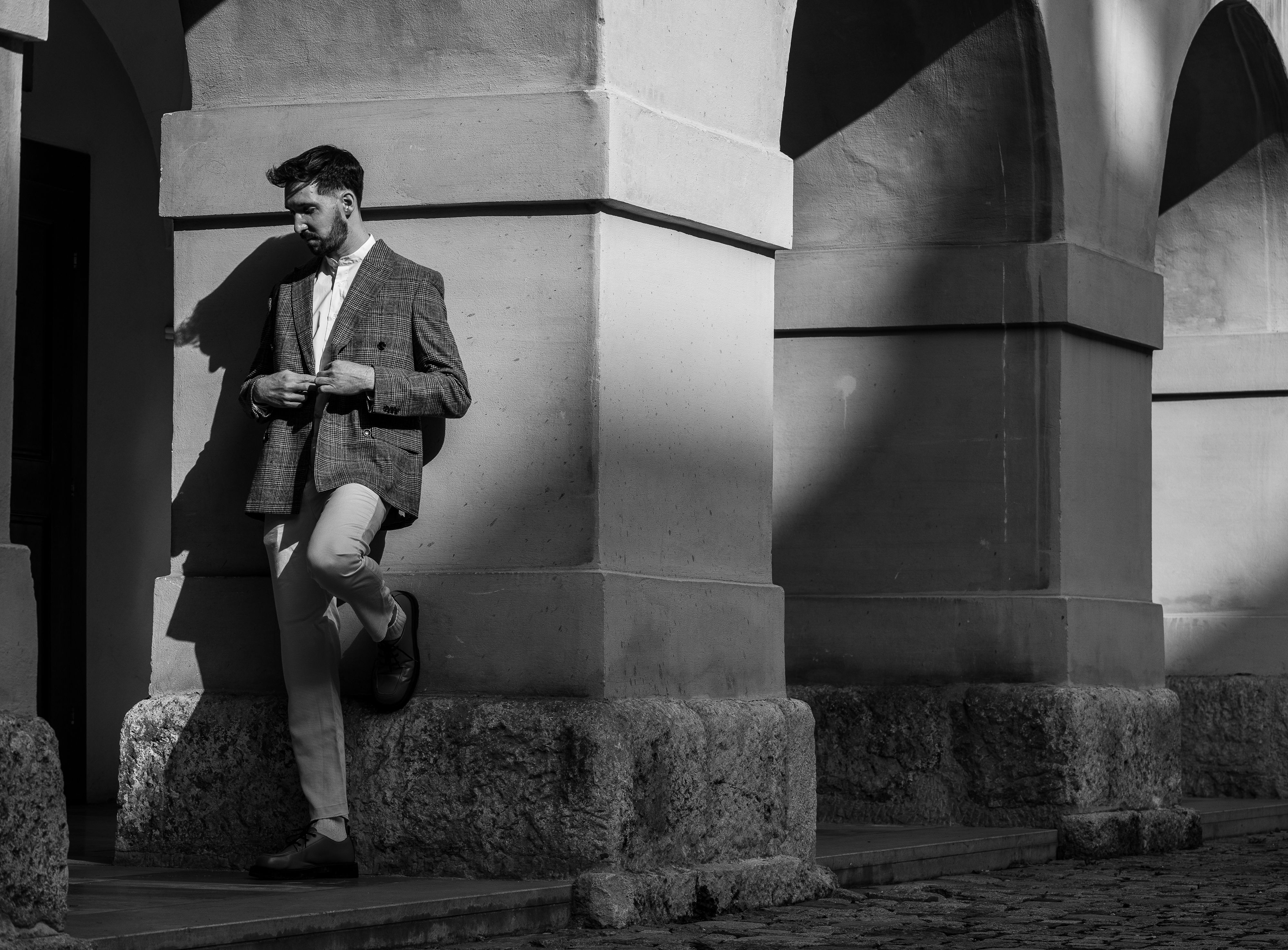 Black and white photo of a stylish man in a suit leaning against a historic building in Graz.