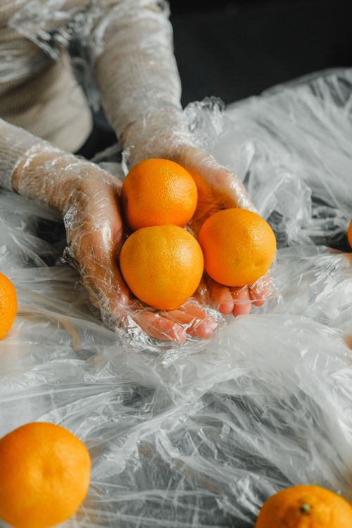 Free Hands wrapped in plastic hold vibrant oranges symbolizing zero waste and sustainability. Stock Photo
