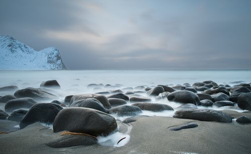 Free A tranquil seascape featuring smooth rocks and misty waves during sunrise on a winter beach. Stock Photo