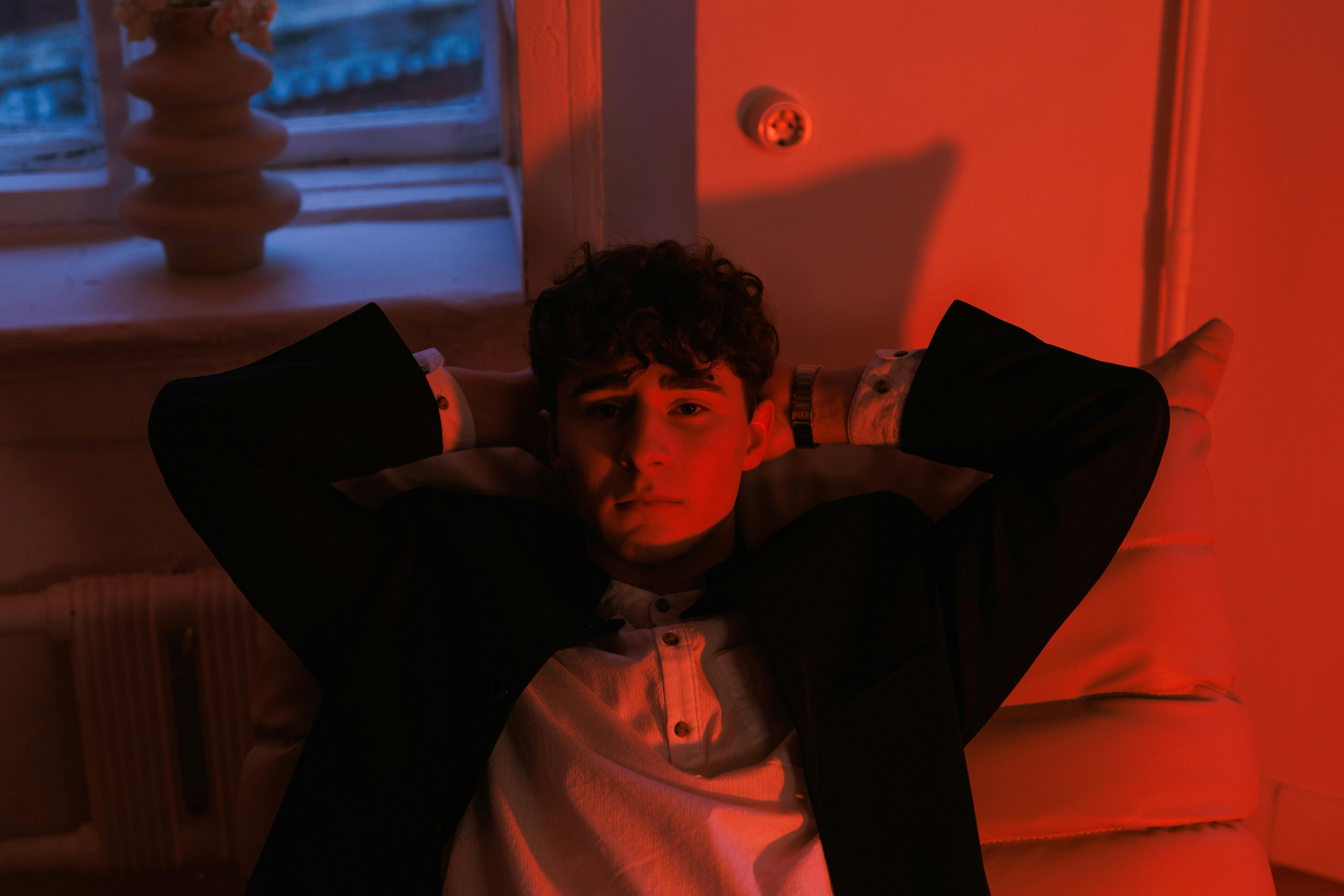 Free Stylish young man in red ambient light, creating a moody and thoughtful atmosphere. Stock Photo