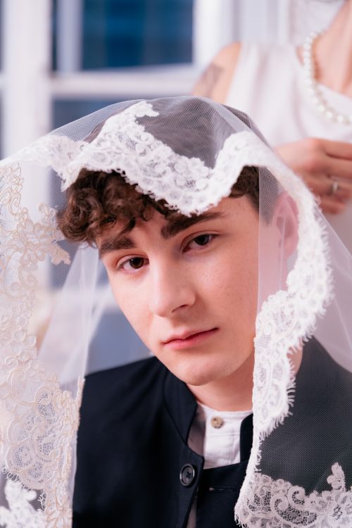 Free A thoughtful young man wears an elegant lace veil, creating a unique and artistic indoor portrait. Stock Photo