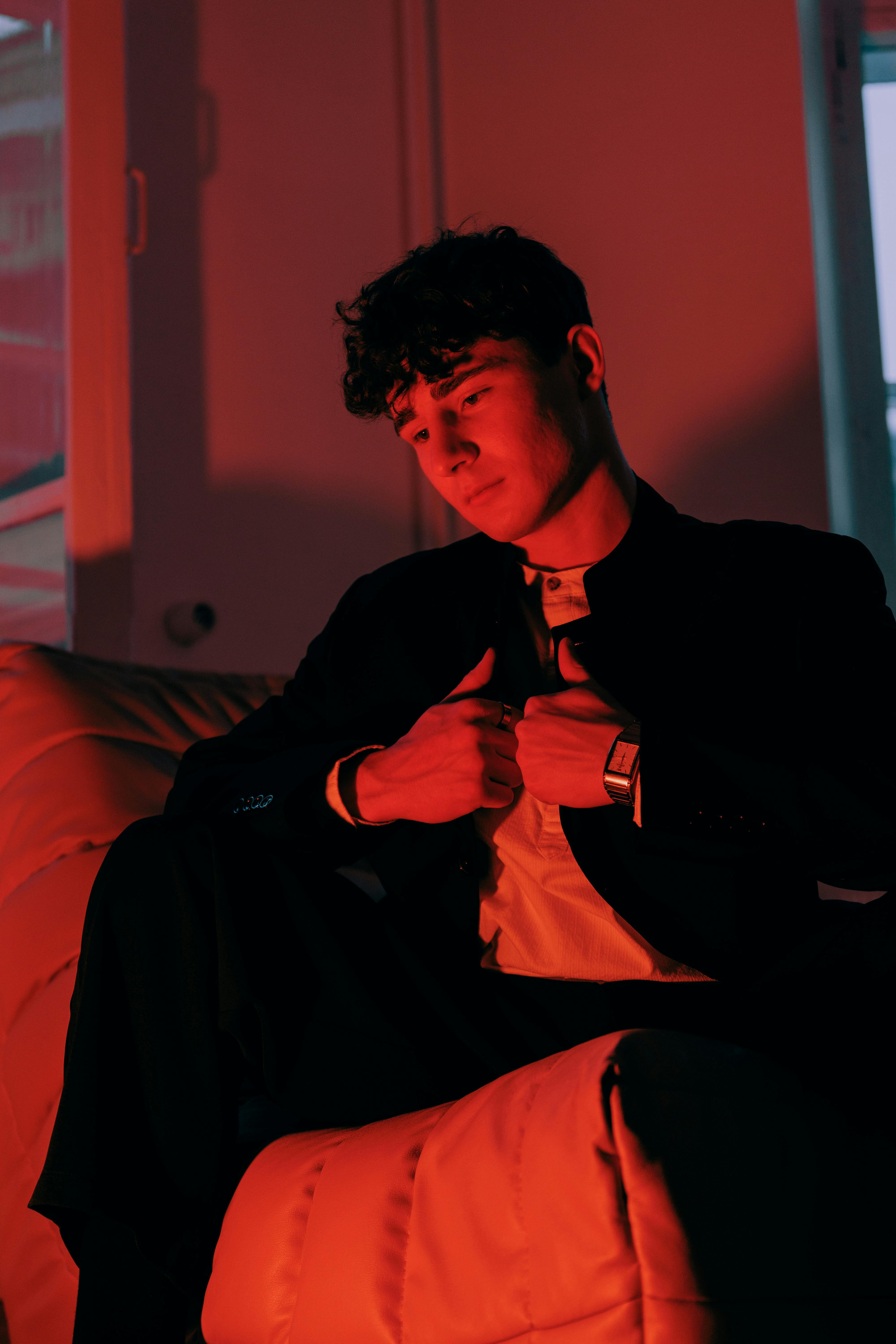 Zadarmo Mladý muž zamyslene sedí v náladovom červenom svetle a vytvára umeleckú atmosféru. Fotka z fotobanky