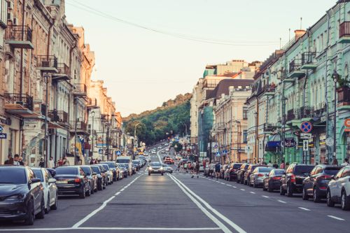 Free Kyiv's Podil district bustling with parked cars and pedestrians on a vibrant summer day. Stock Photo