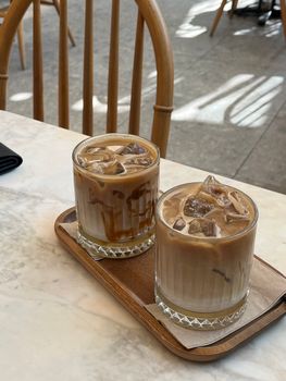 Two glasses of iced coffee on a wooden tray in a bright cafe setting.