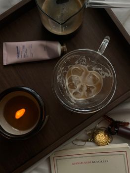 Aesthetic flat lay with coffee, skincare, candle, and book on a tray.