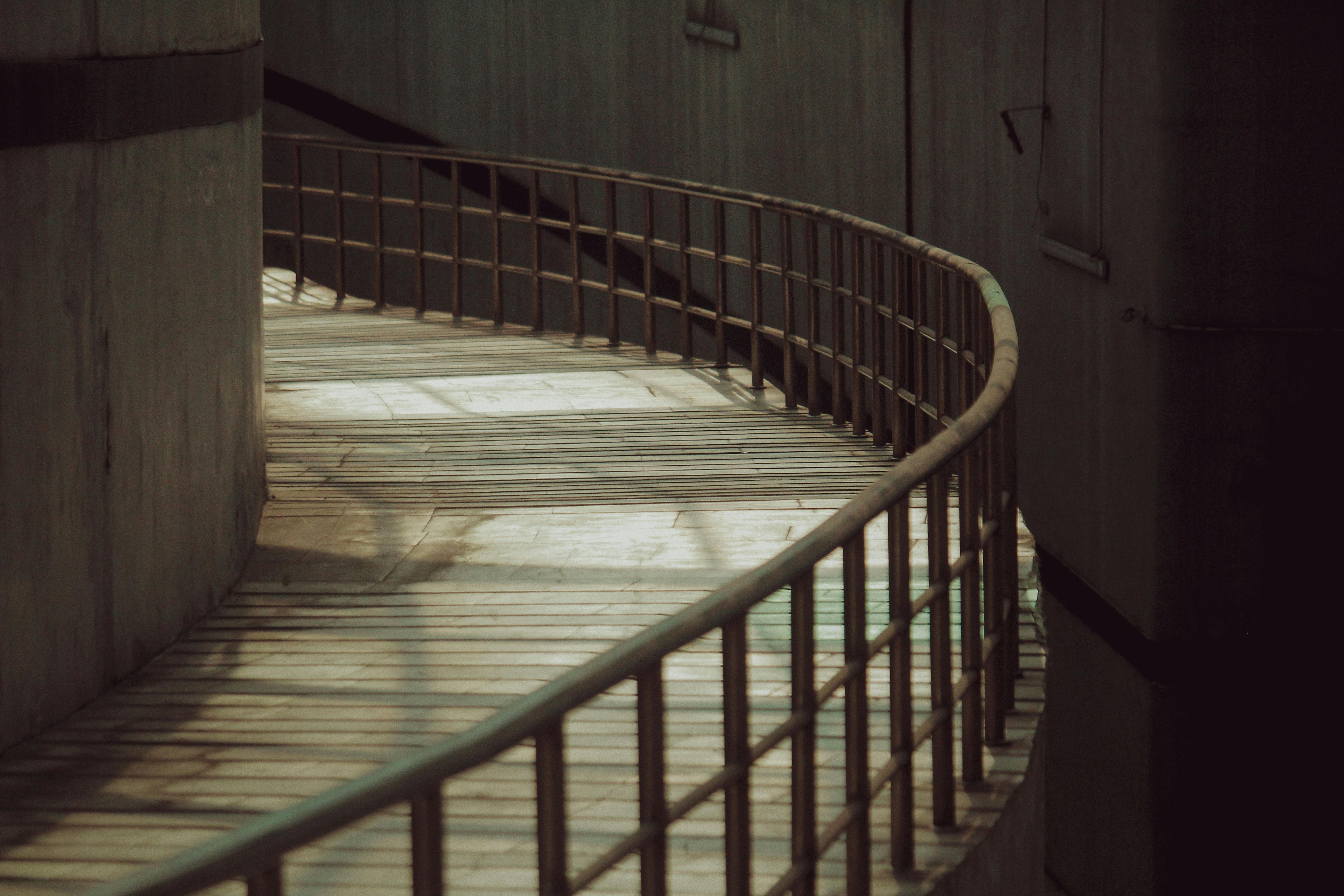 Free A curved wooden pathway with railings in an industrial urban environment, casting shadows. Stock Photo