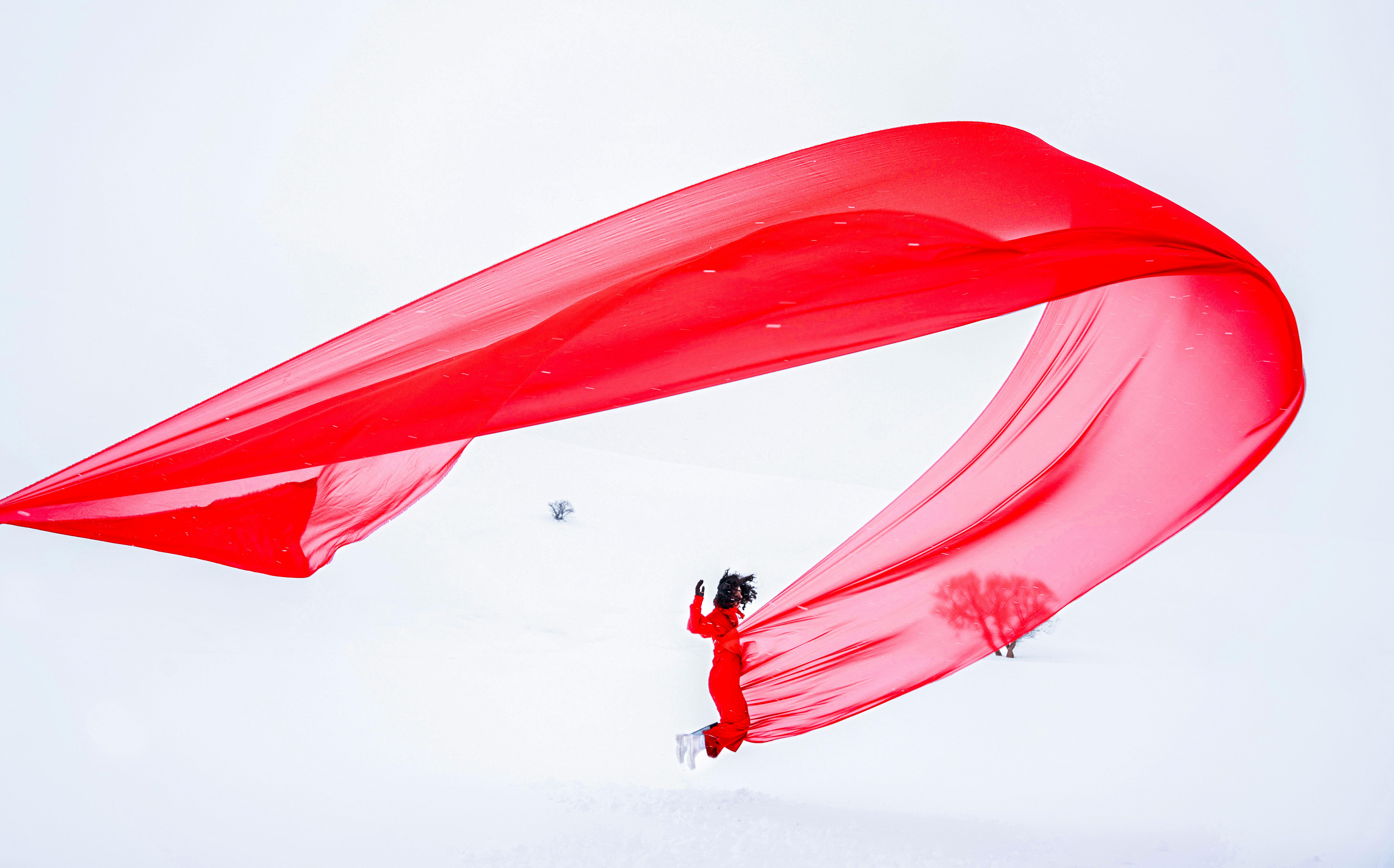 Gratuit Une personne vêtue de rouge, avec un tissu flottant, sur un terrain enneigé, créant un contraste visuel dynamique. Photos