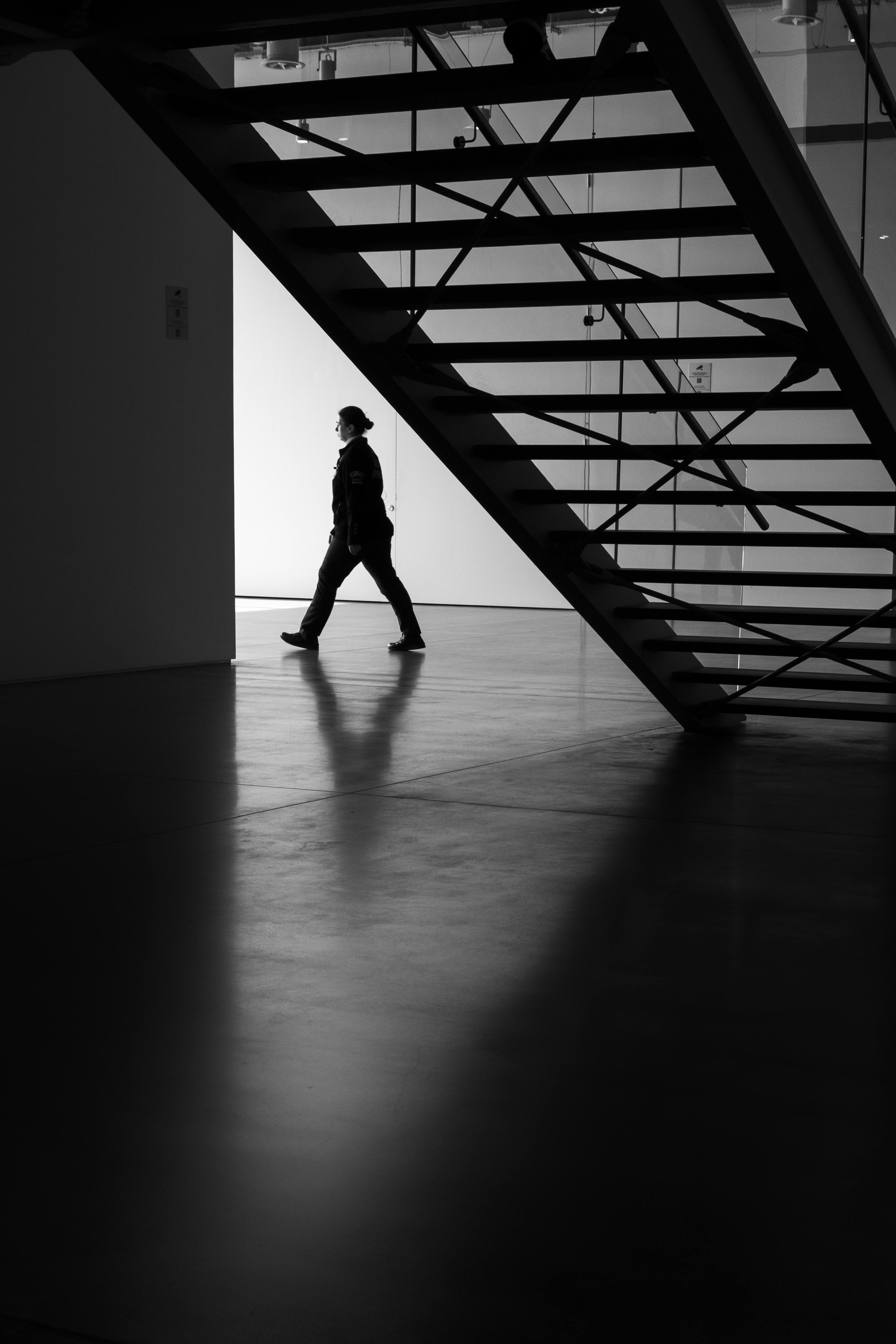 Gratuit O persoană în siluetă merge pe sub o scară modernă într-un spațiu interior artistic, minimalist. Fotografie de stoc