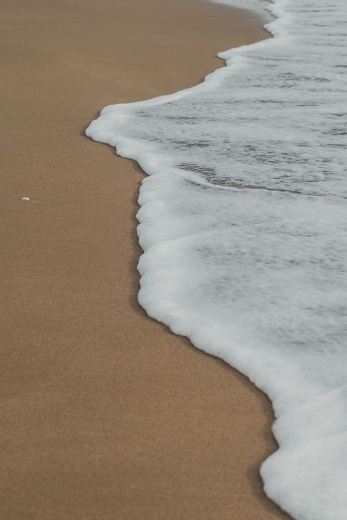 Free A serene view of ocean waves softly breaking on a sandy beach. Stock Photo