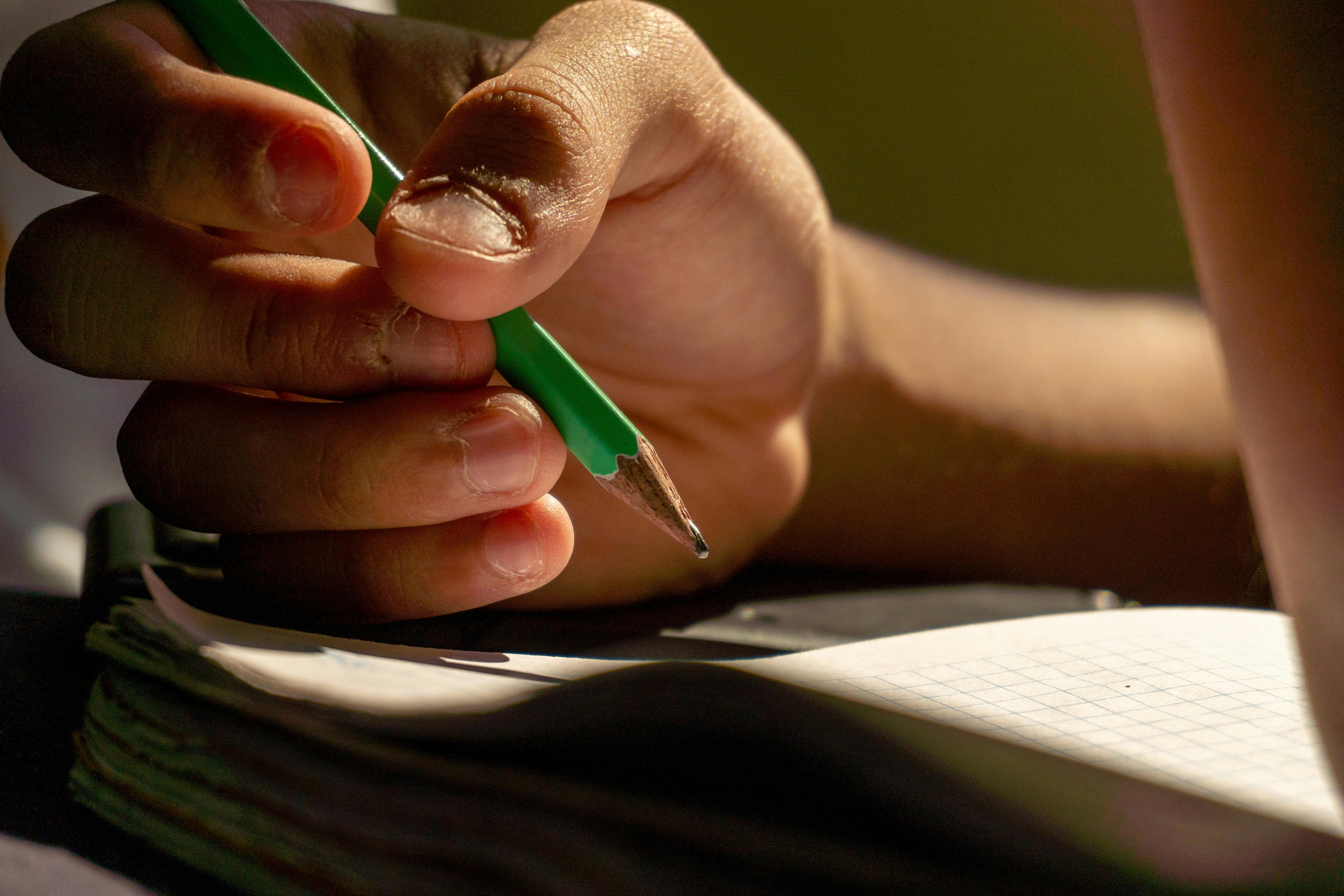Gratis Vista detallada de una mano escribiendo con un lápiz en un cuaderno, lo que implica estudio o creatividad. Foto de stock
