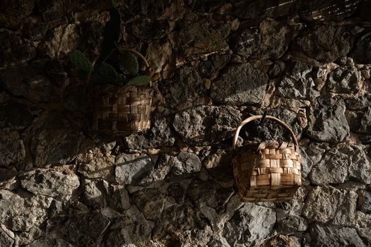 Woven baskets hanging on a rustic stone wall with dramatic shadows, evoking a natural earthy feel.