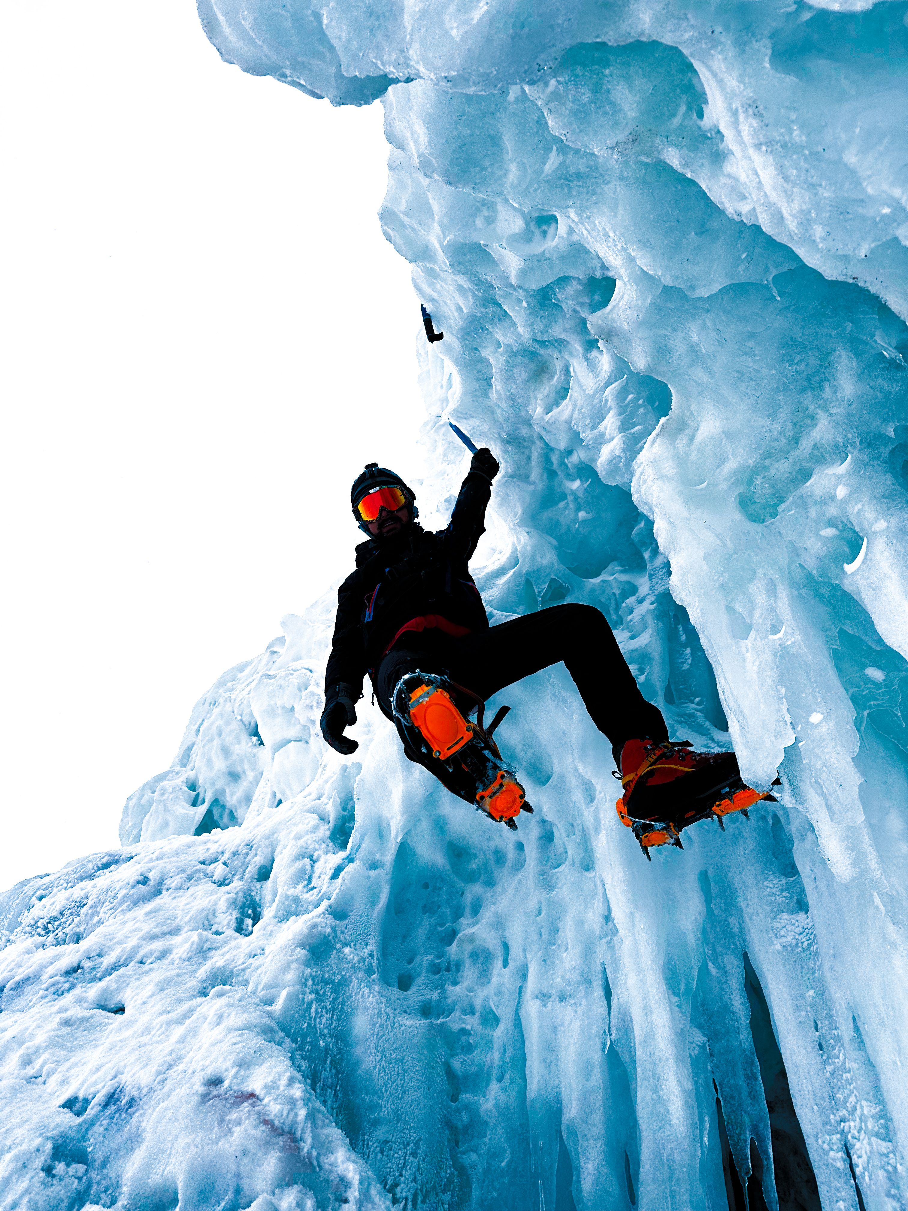 Daring climber ascends icy cliff with gear during a clear winter day, showcasing extreme sports.