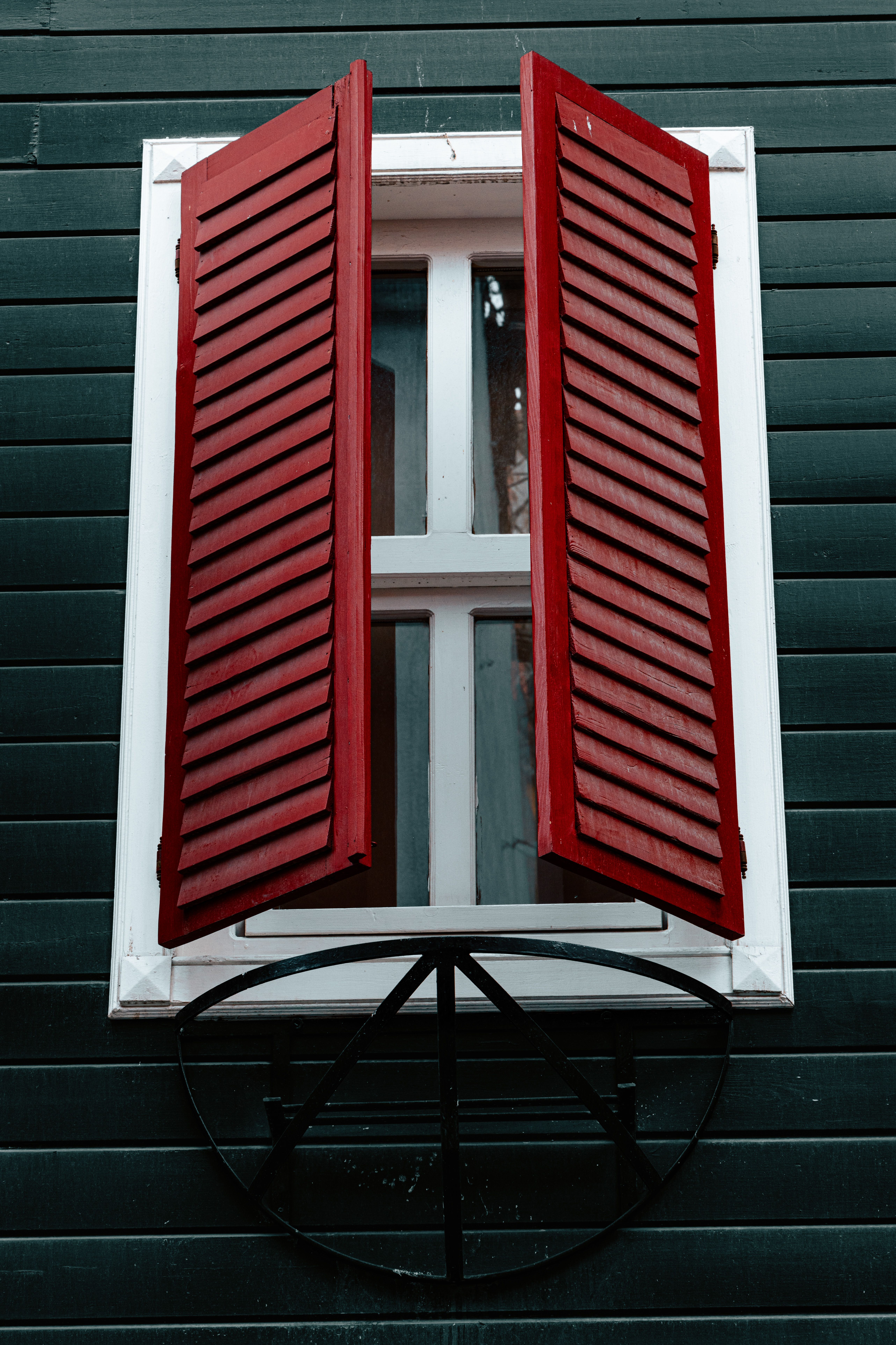 Red shutters on a green wooden wall create a striking contrast and focal point.