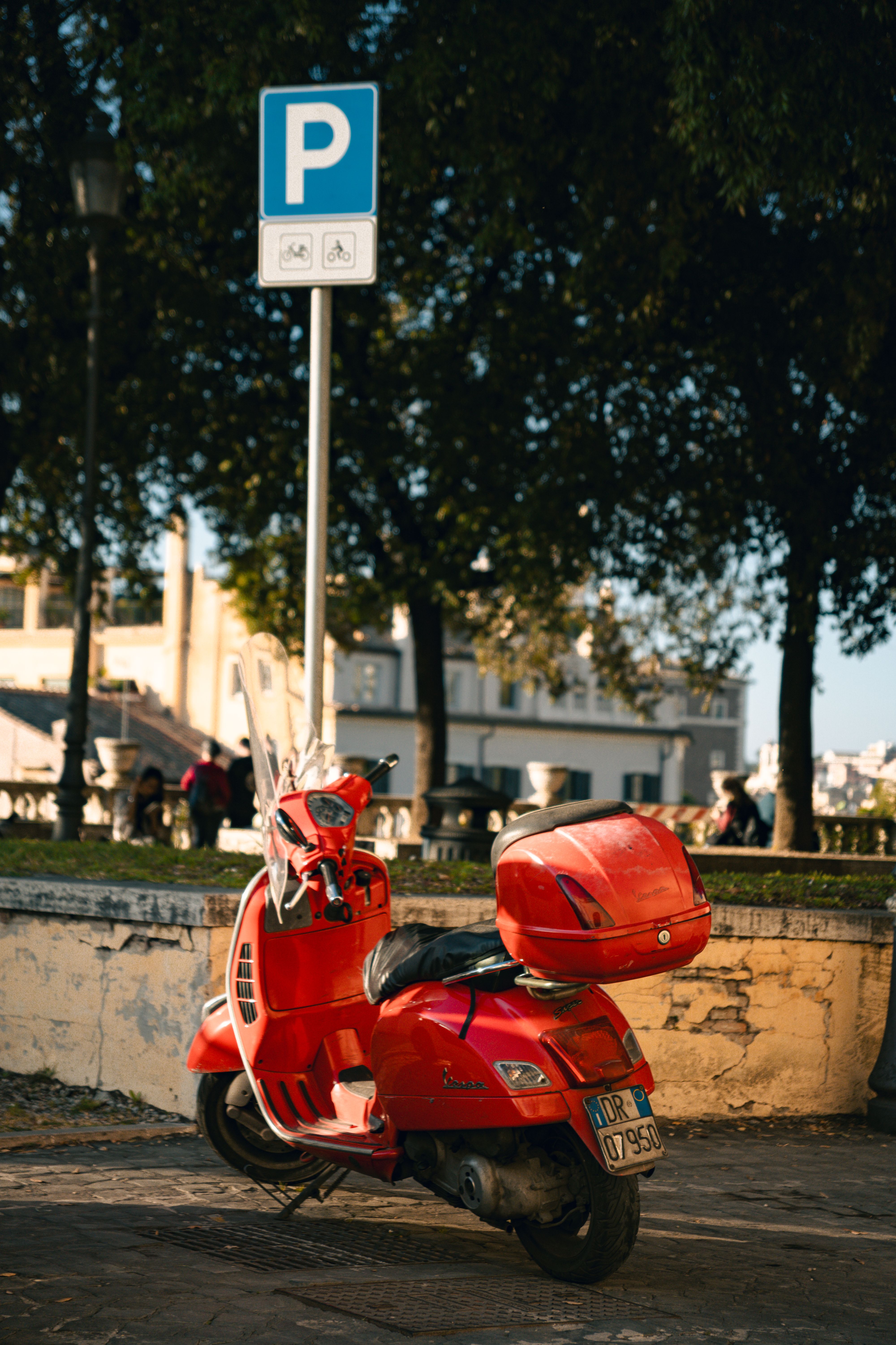 A vibrant red scooter parked under a sign in sunny Rome, Italy, showcasing Italian city life.