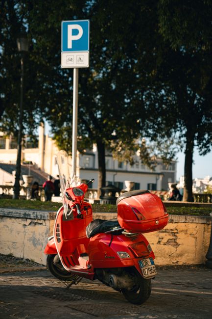 A vibrant red scooter parked under a sign in sunny Rome, Italy, showcasing Italian city life.