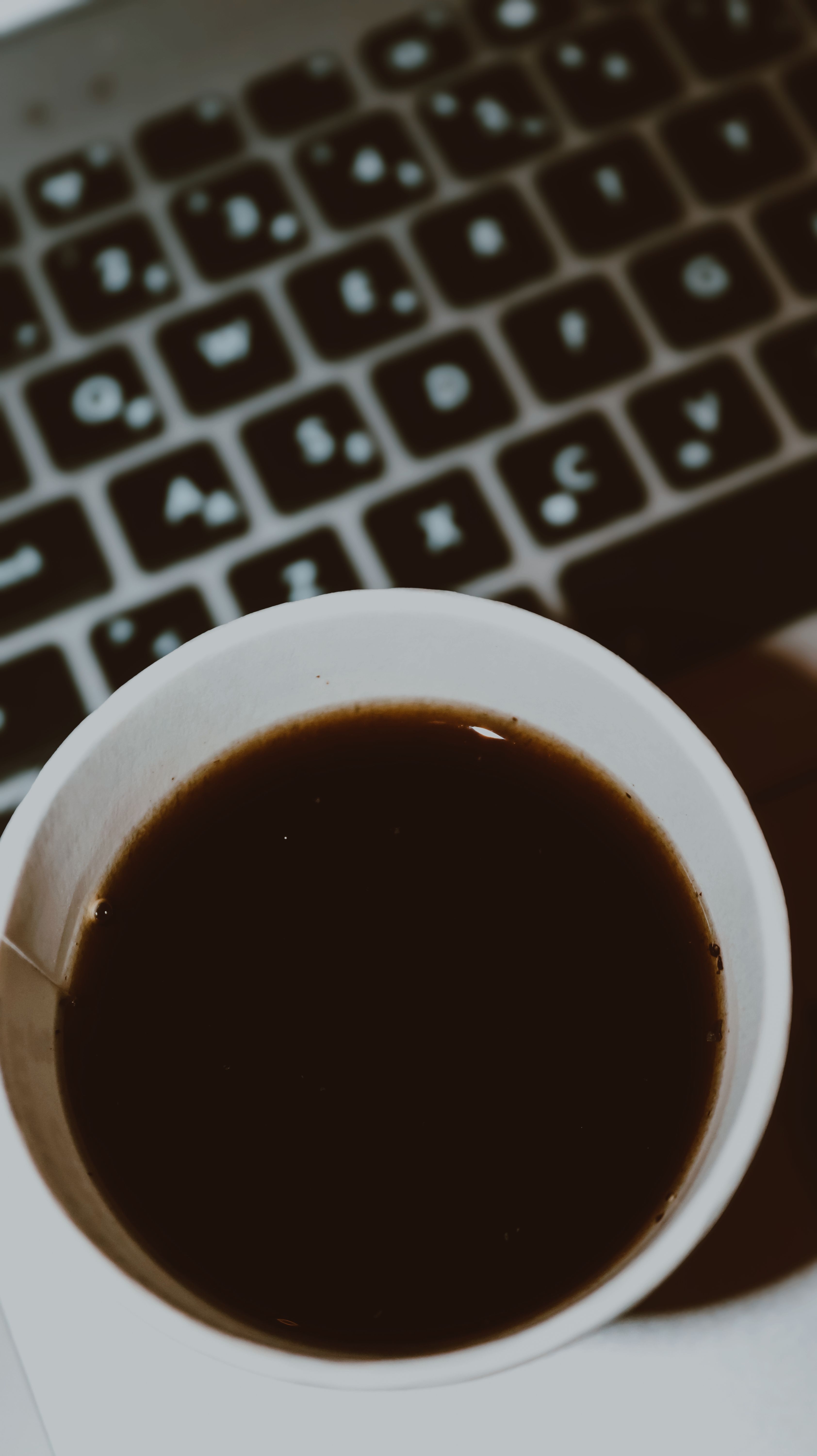 A cup of coffee placed in front of a laptop keyboard, captured with a moody tone.
