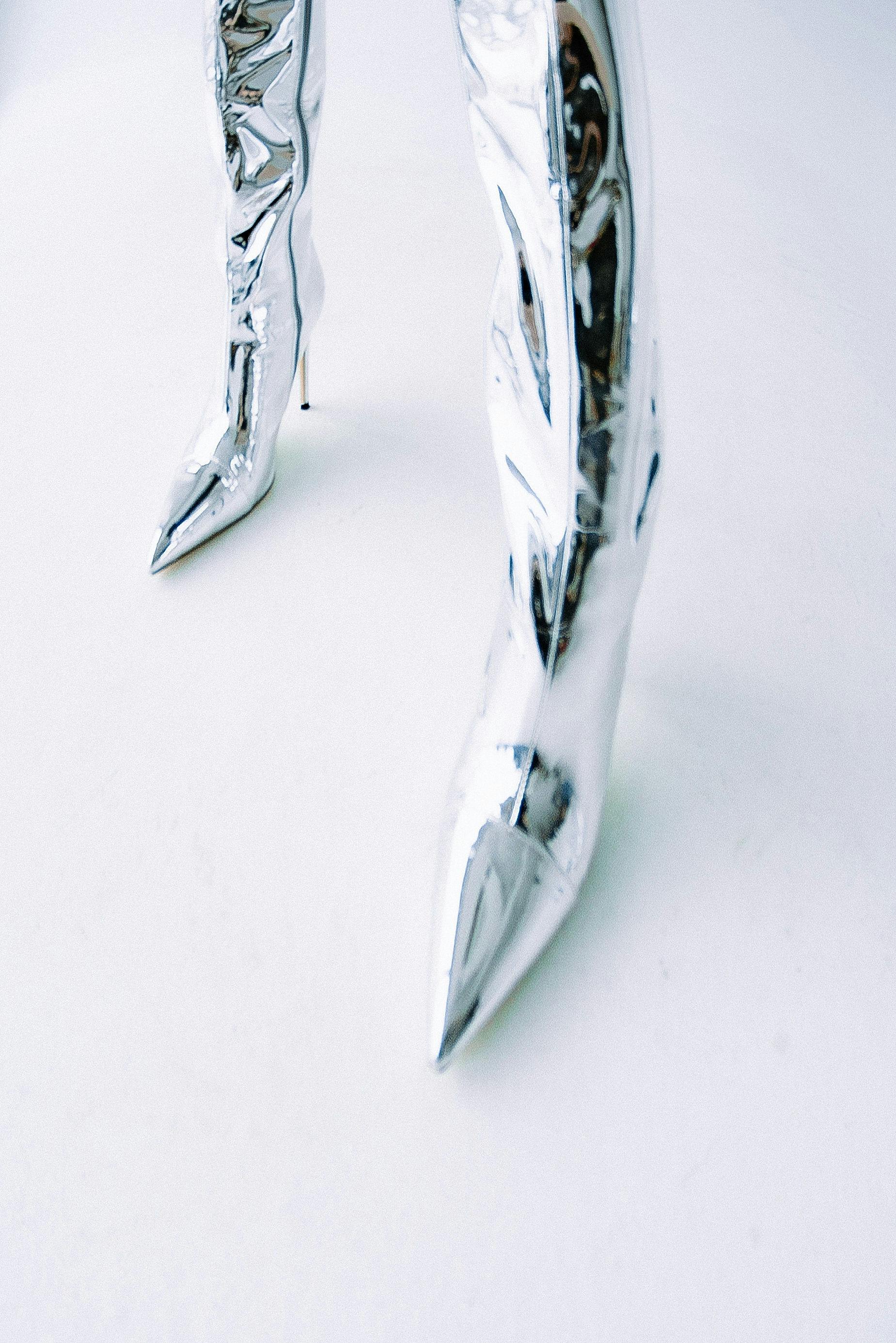 Gratis Elegantes botas de tacón alto plateadas exhibidas sobre una superficie blanca limpia, enfatizando la moda moderna. Foto de stock