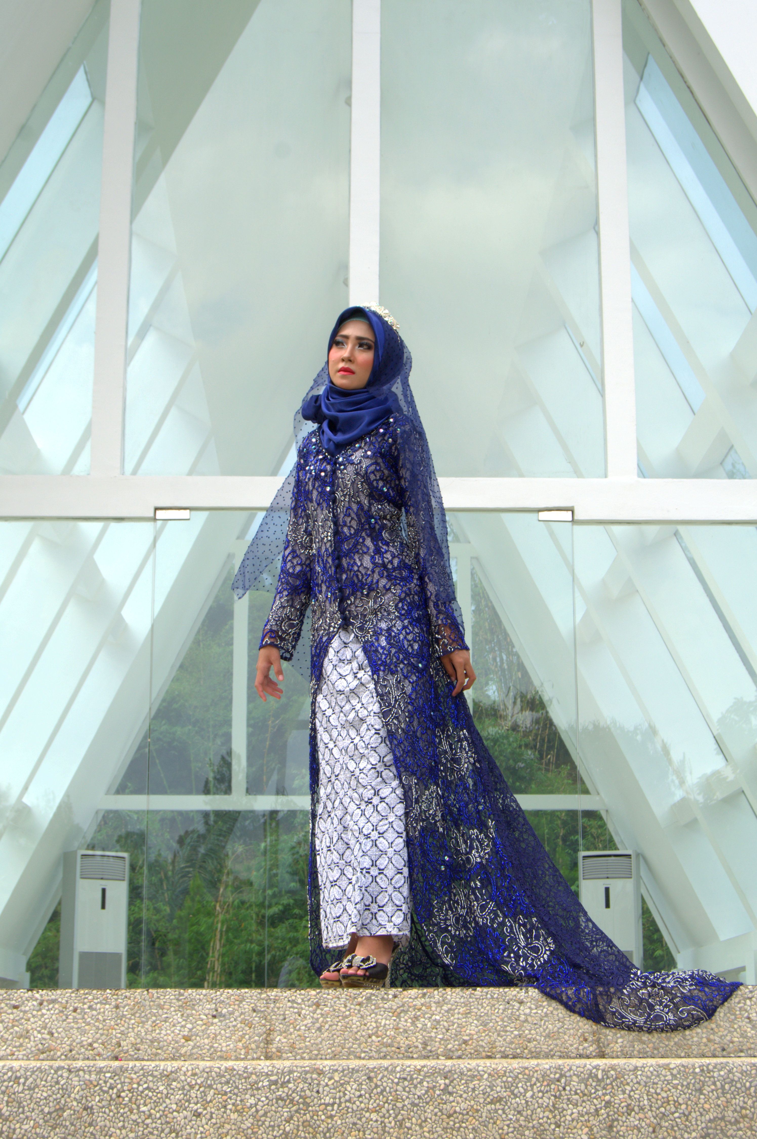 Stylish woman in blue hijab dress standing outside a modern building in Bandung, Indonesia.